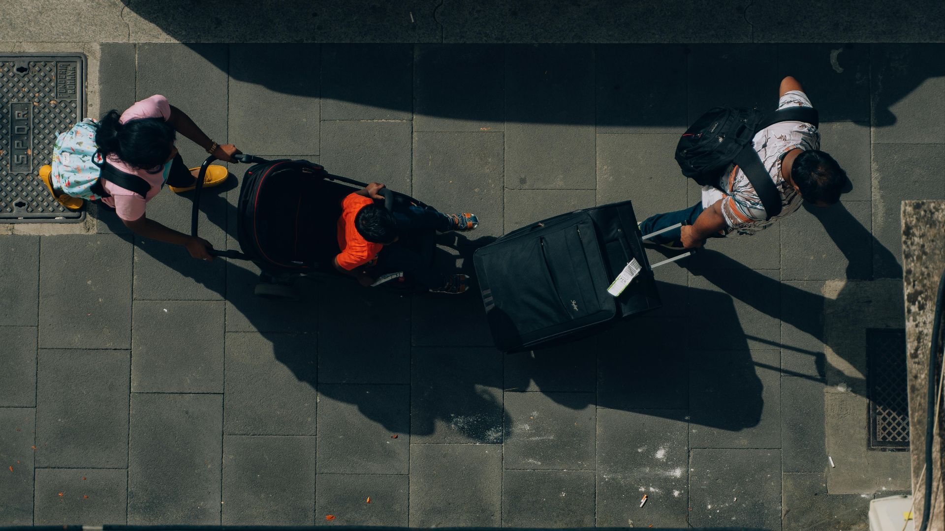 Aerial view of travelers with luggage and a stroller on a Rome street.