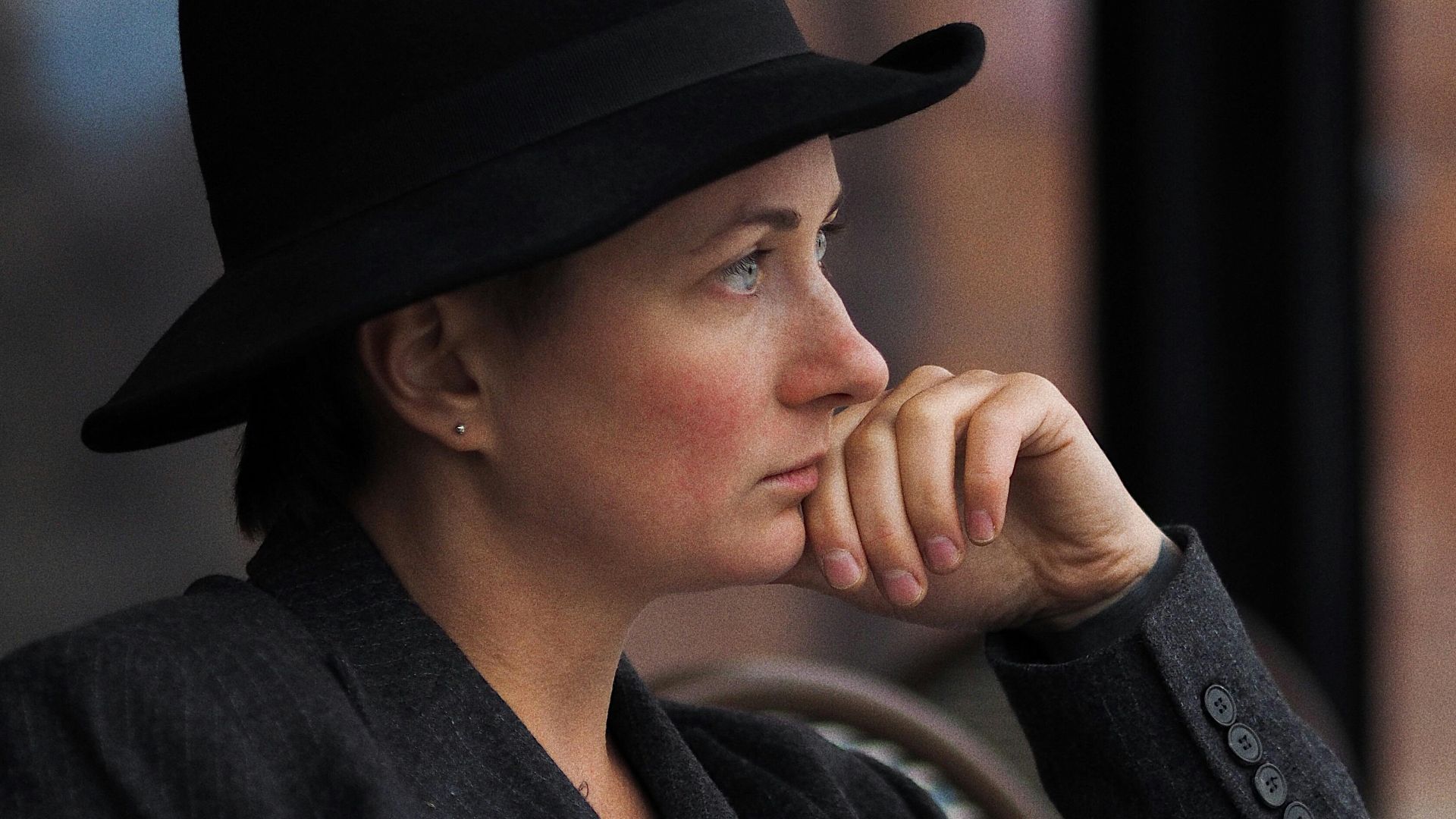 Side view of a woman wearing a black hat and blazer, in deep thought.
