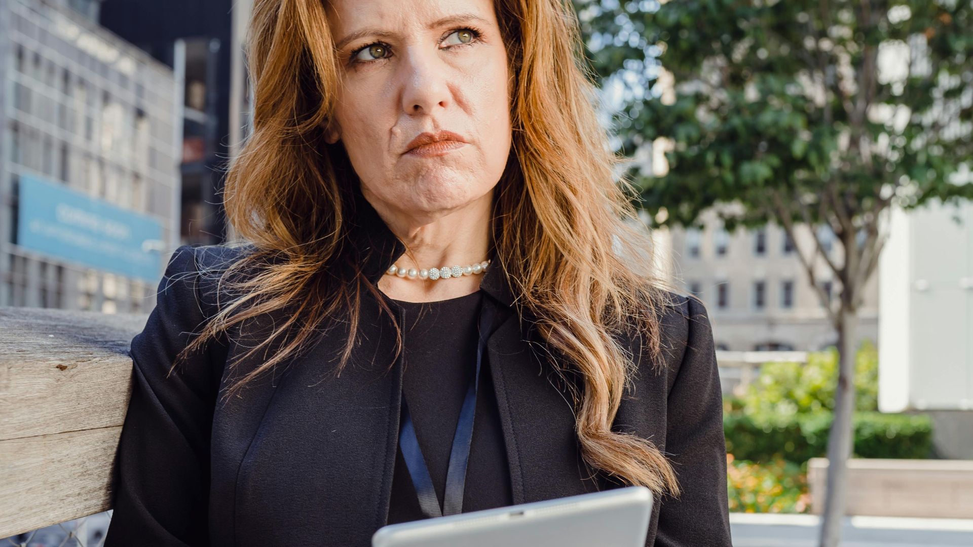Thoughtful businesswoman using tablet outside modern office building.