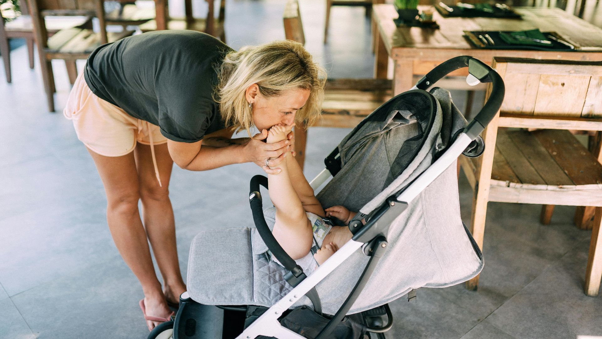 A mother kissing her baby in a stroller at an outdoor dining area, expressing love.