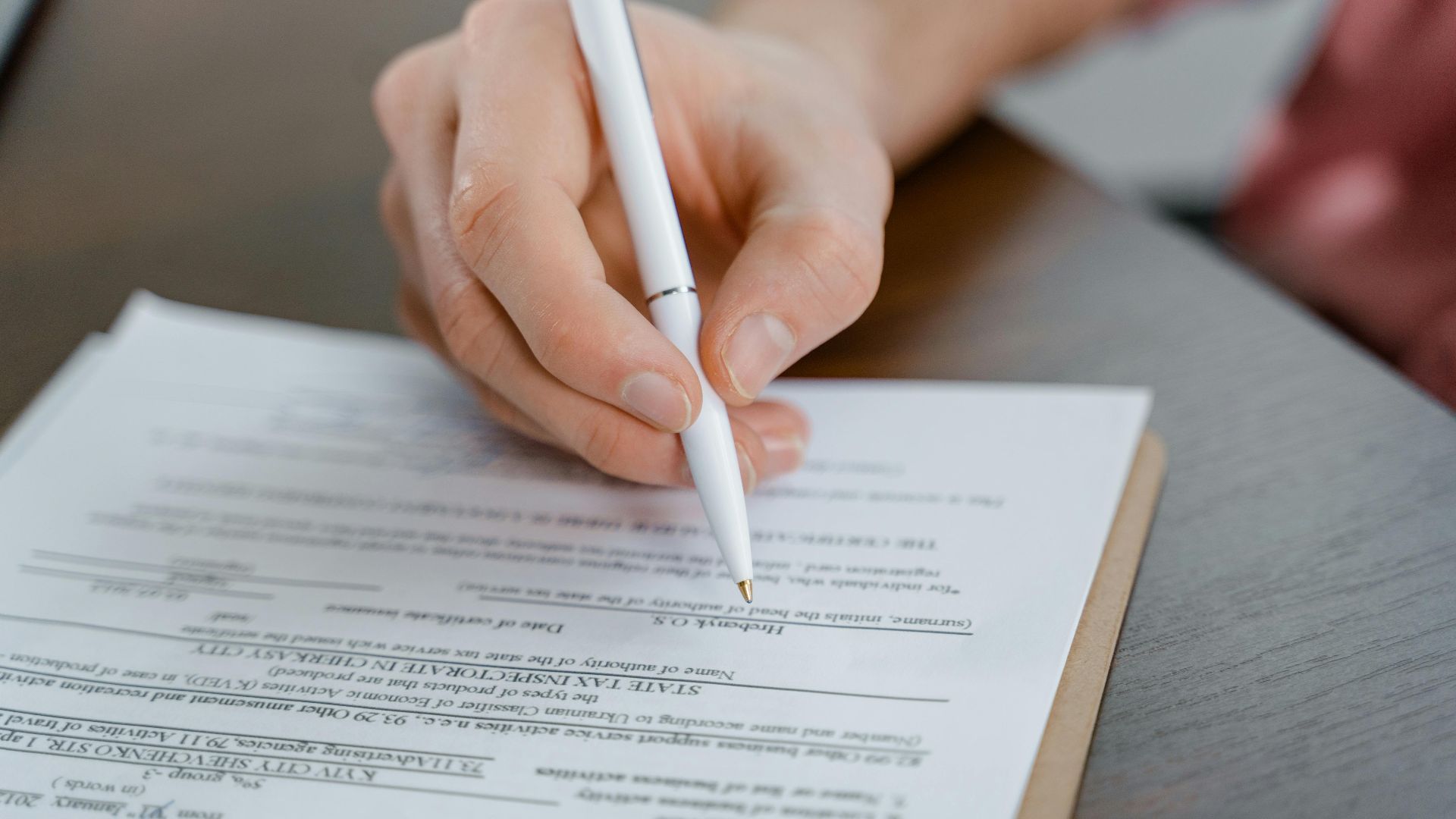 A hand holding a pen signing a document, close-up shot with focus on the paper.