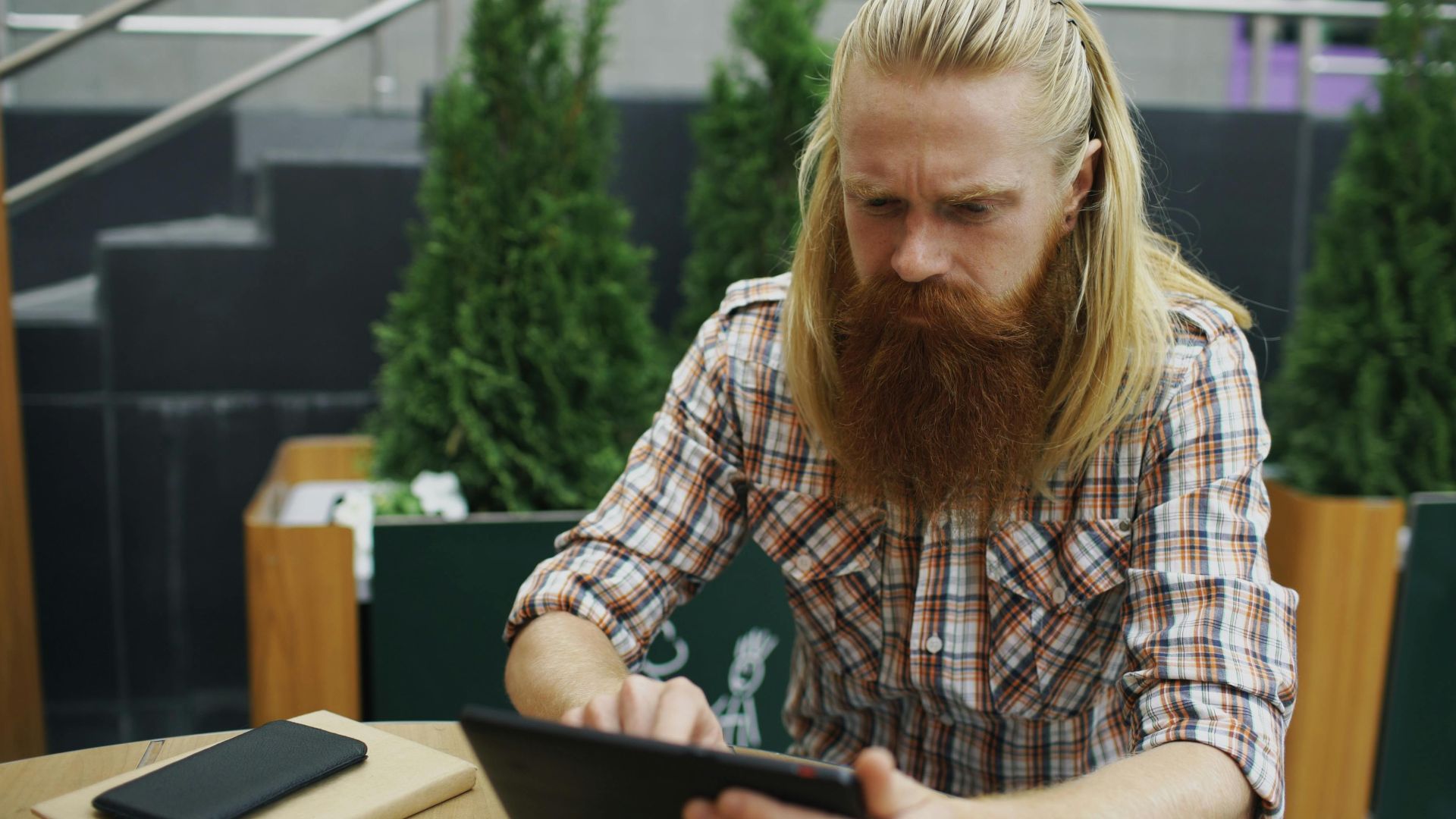 Focused man with long hair and beard using a tablet at an outdoor cafe setting.