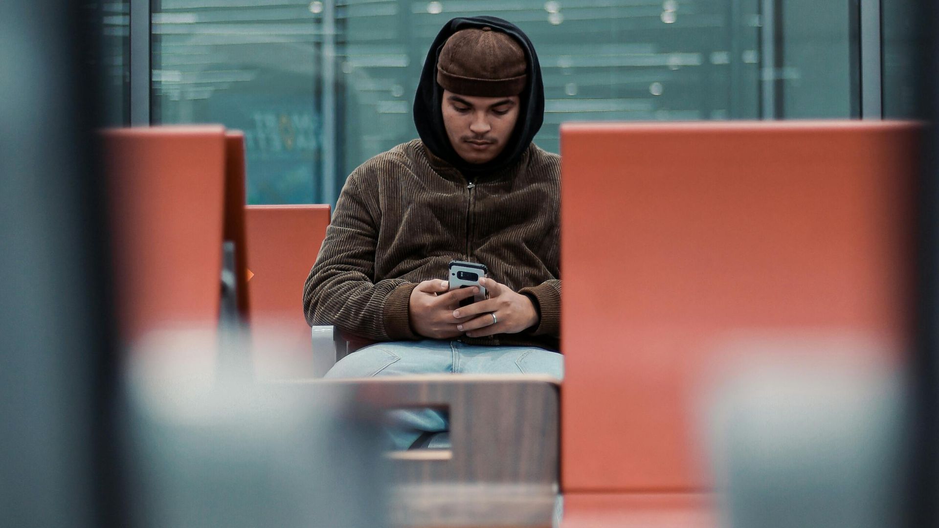 Young man sitting in an airport lounge in Rabat, Morocco, using a smartphone. Modern and relaxed setting.