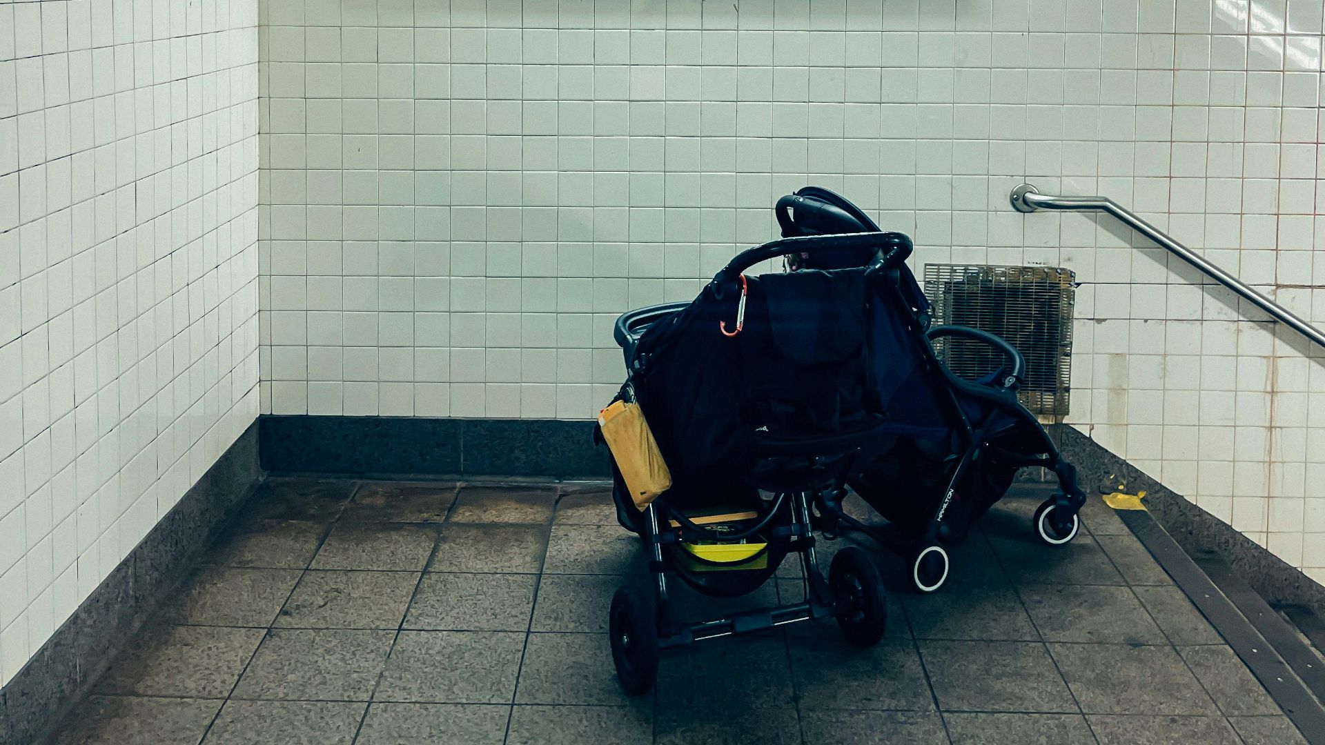 An empty New York subway station with a baby stroller beneath directional signs to Brooklyn and The Bronx.