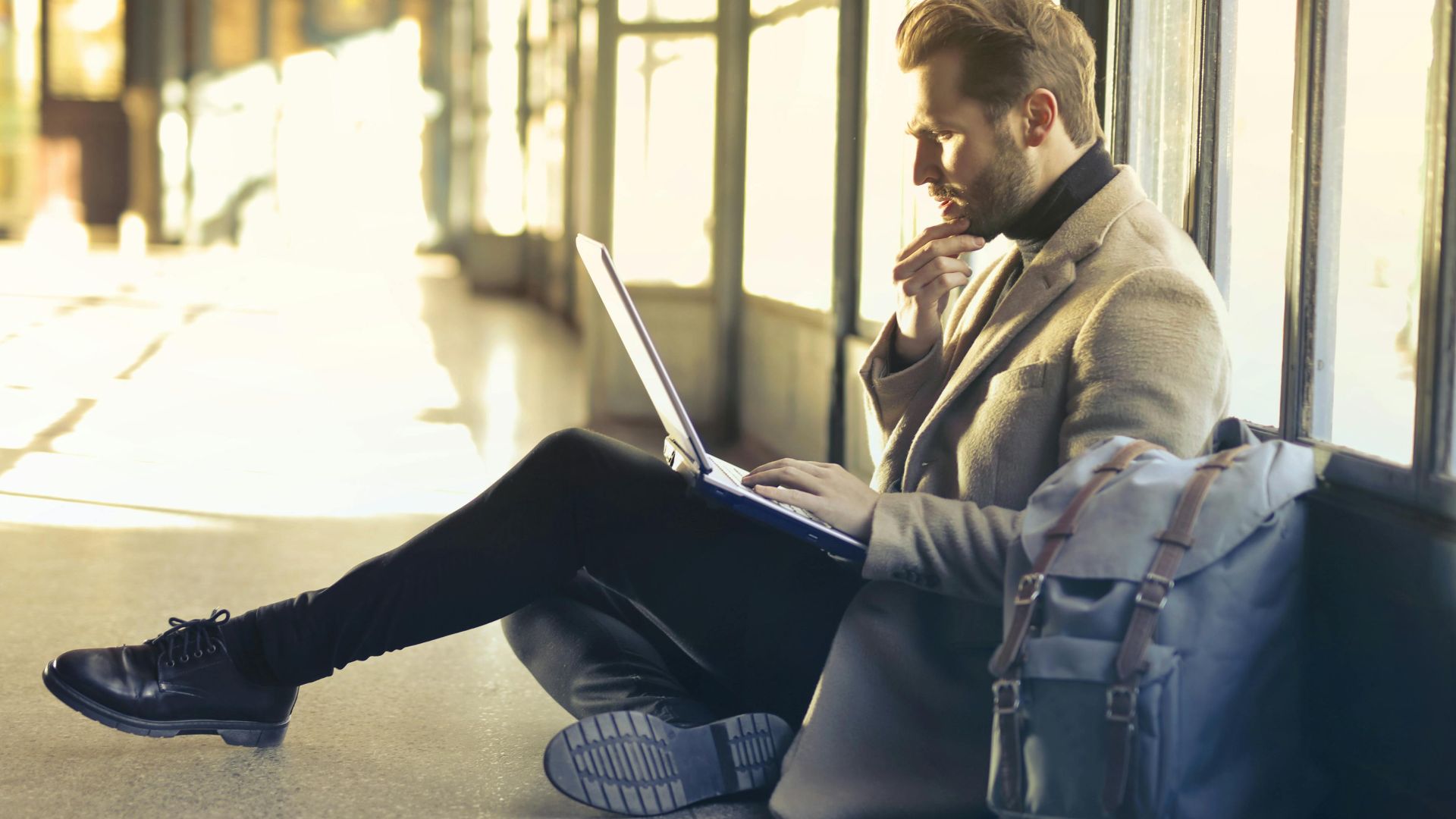 Young man sitting indoors at an airport using laptop. Ideal for remote work themes.