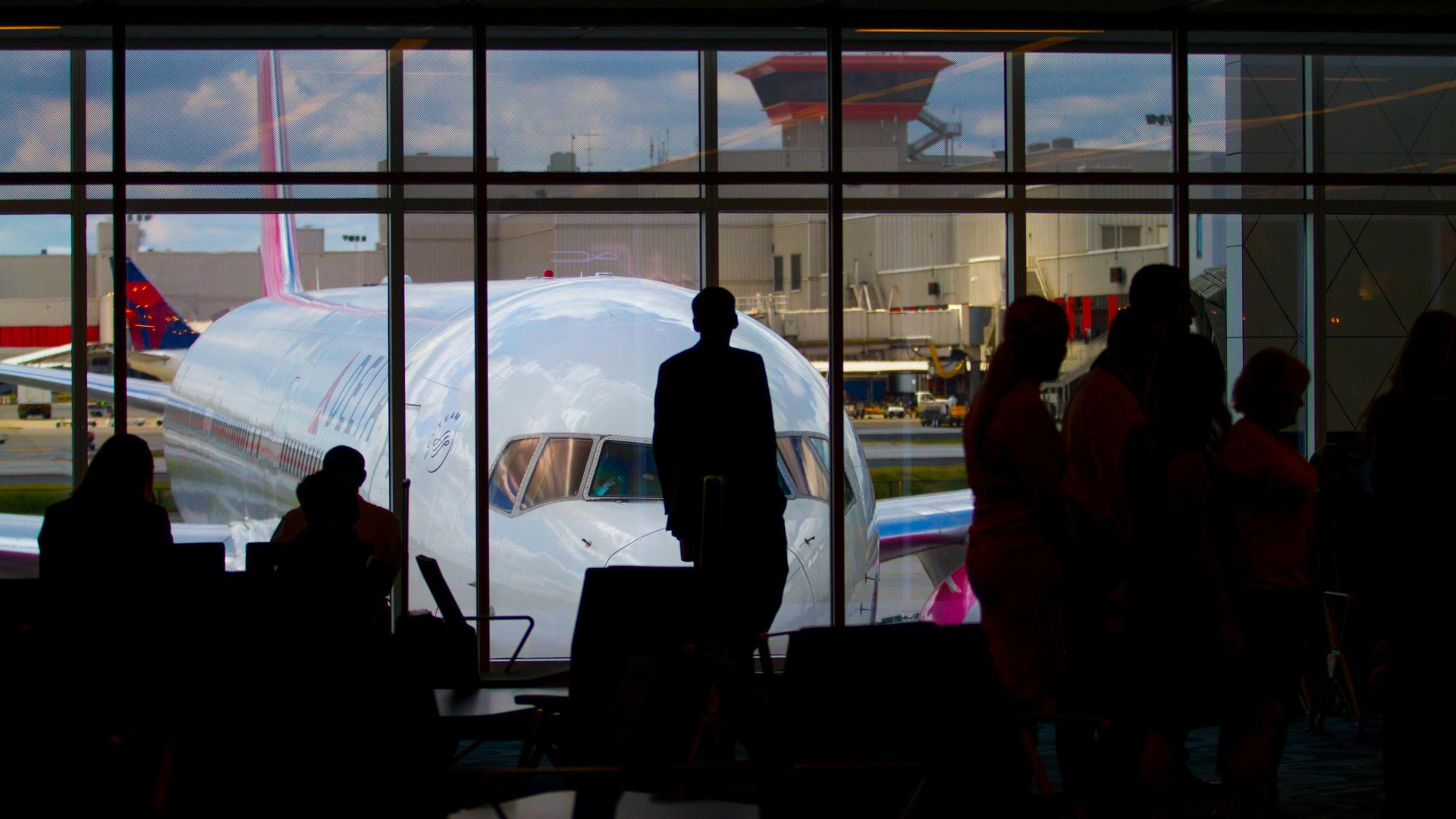 Silhouettes of travelers waiting at an airport terminal with an airplane visible through the window.