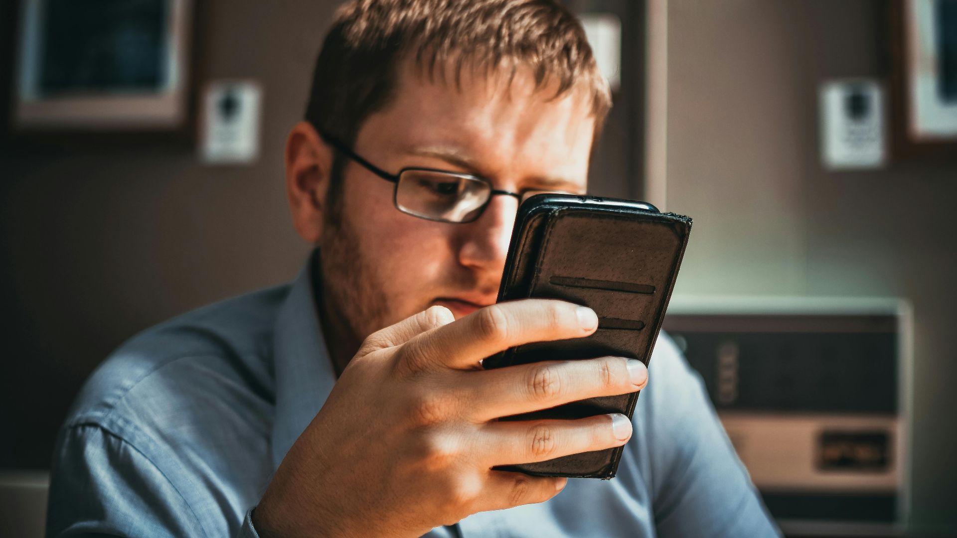 Serious businessman wearing glasses focused on smartphone in a modern office setting.