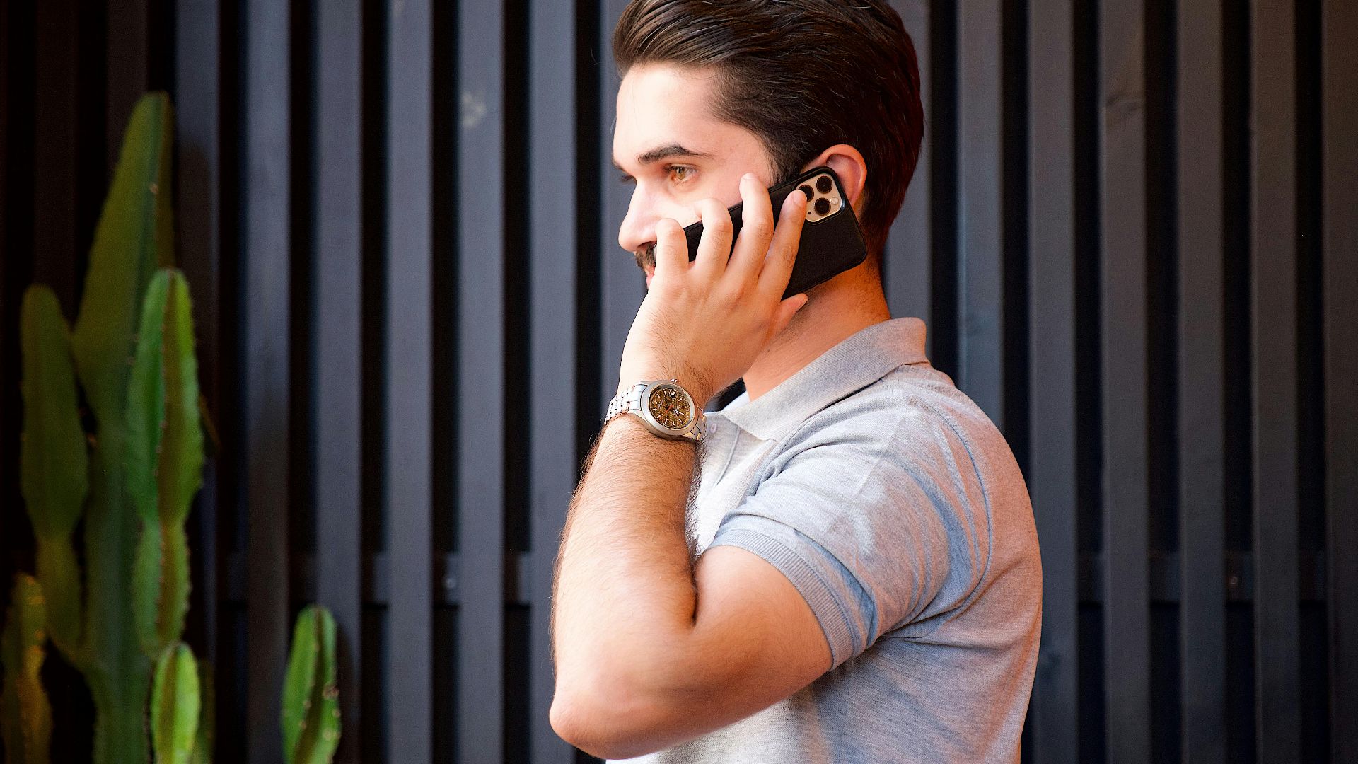 A young man in a casual shirt communicates on a smartphone while wearing a wristwatch.