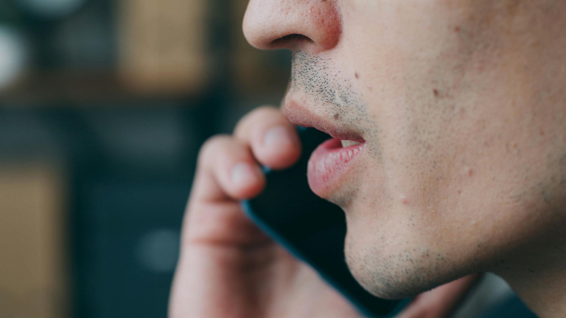 Side profile of an adult speaking on a smartphone indoors.