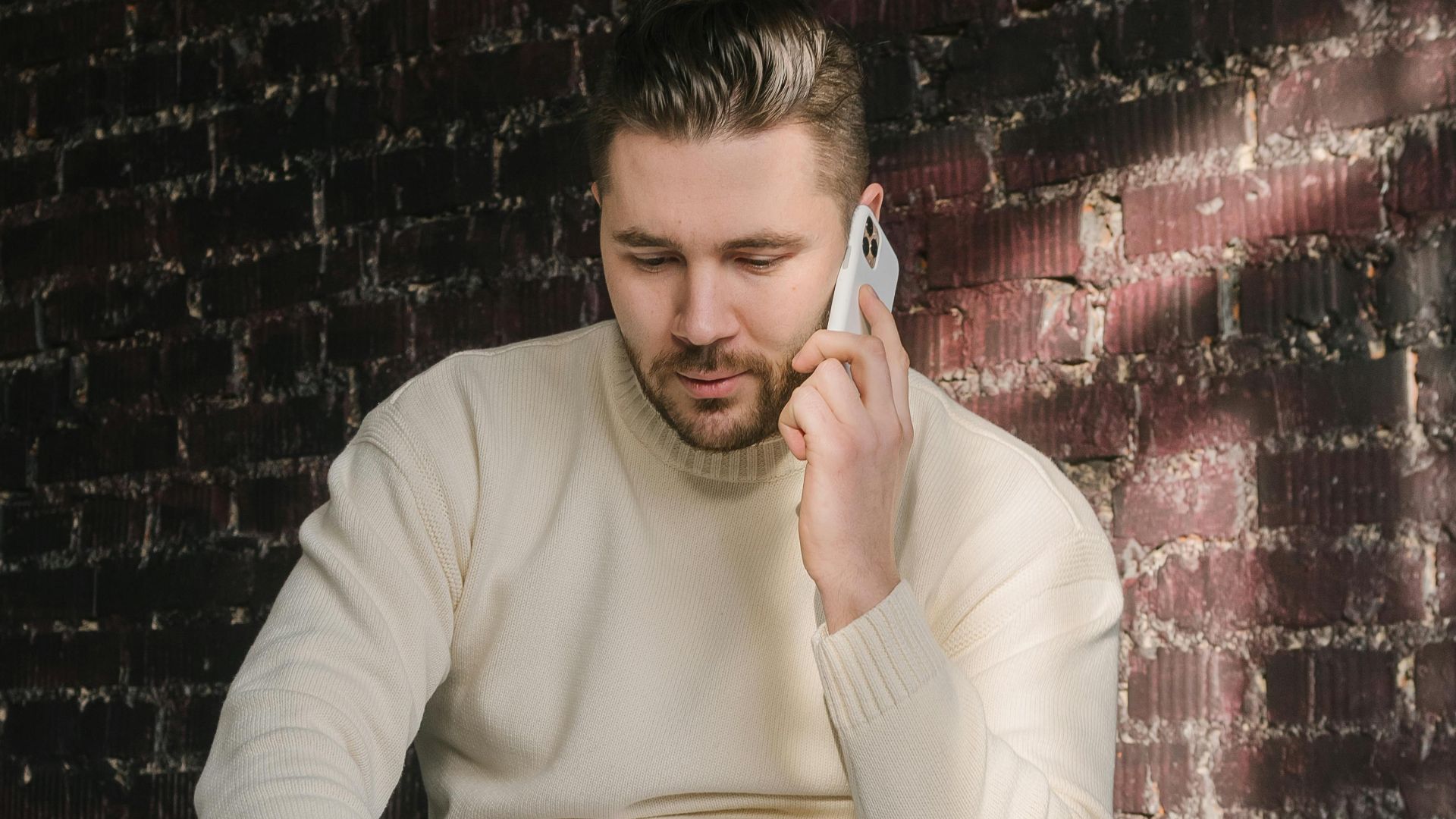 Man in casual attire engaged in a remote work setup, seated on a bed with a laptop and smartphone.