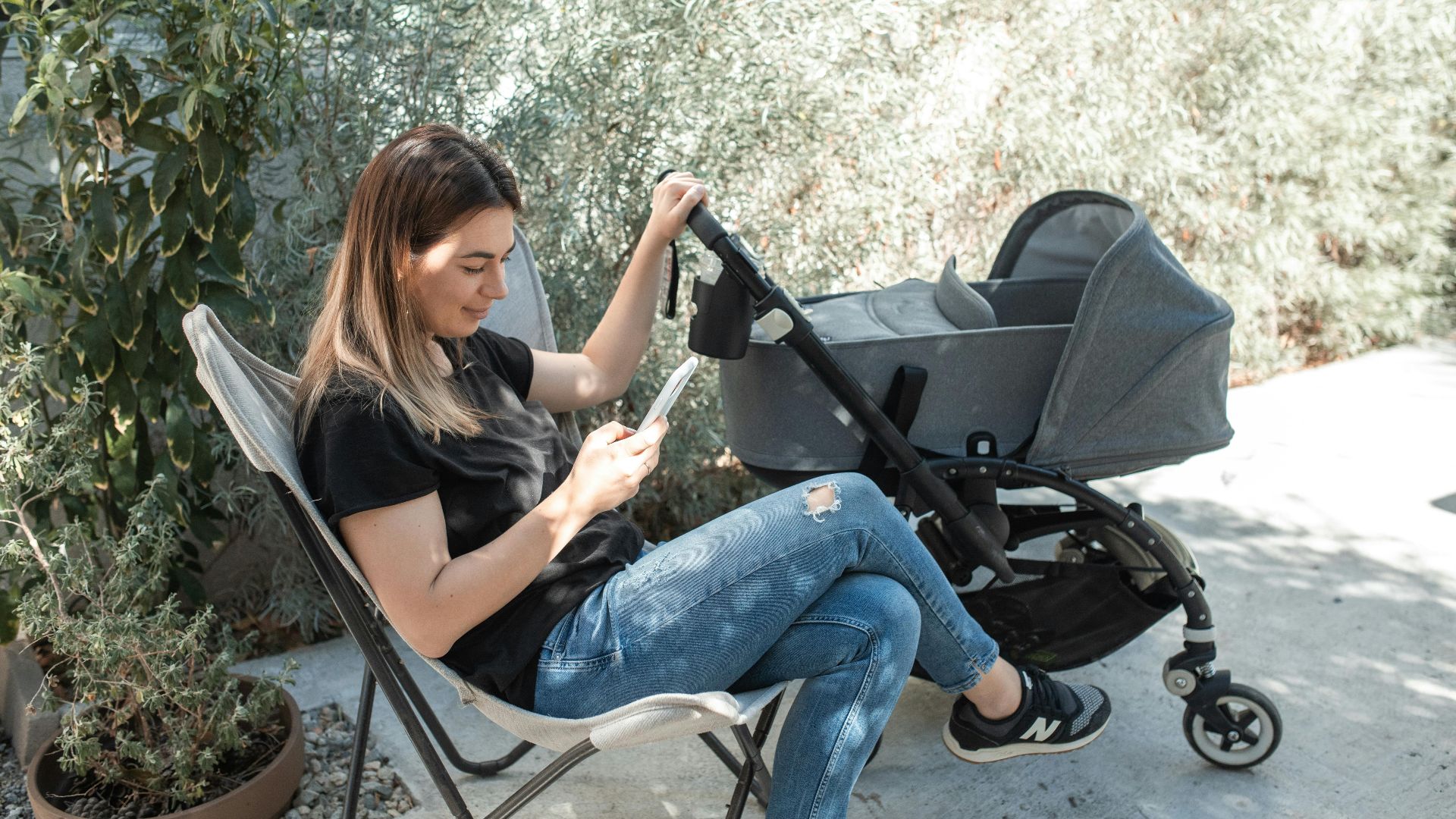 A woman enjoying her break outdoors, sitting near a stroller, using a smartphone.