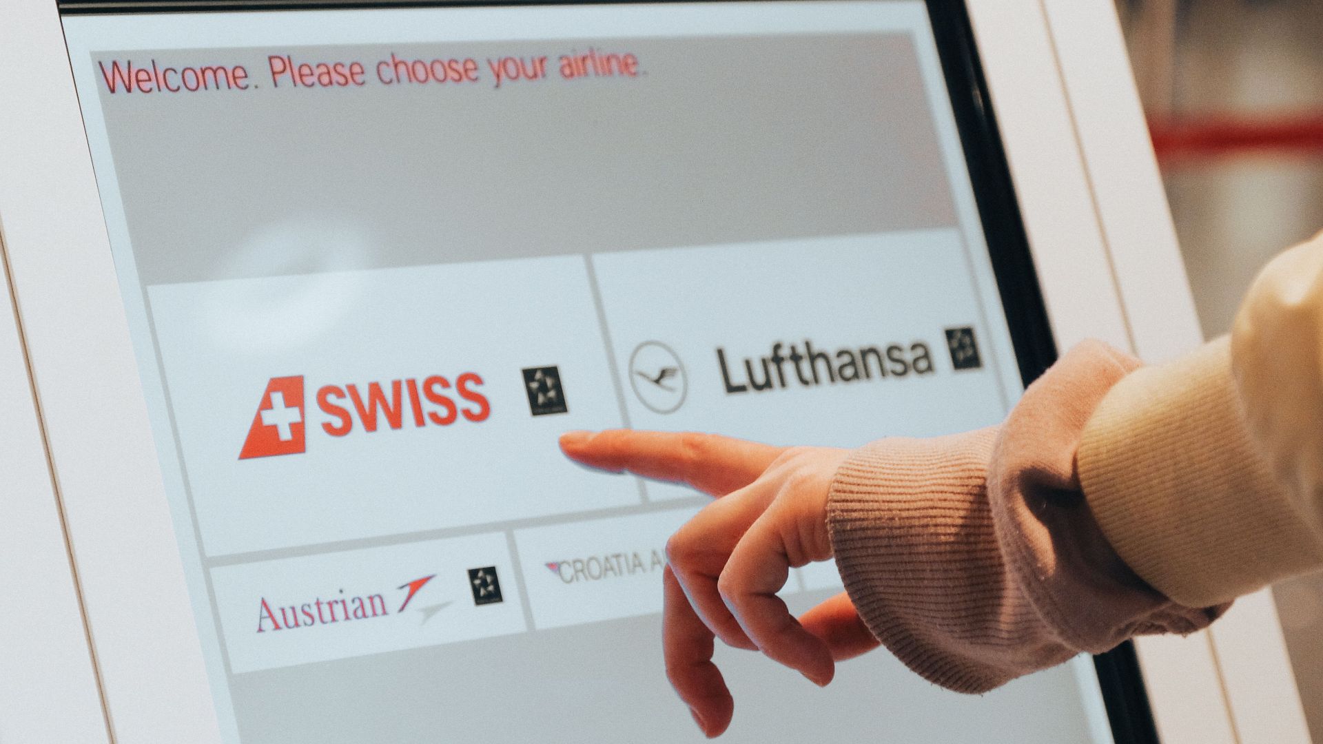 Hand interacting with airport kiosk for airline selection. Modern travel technology.