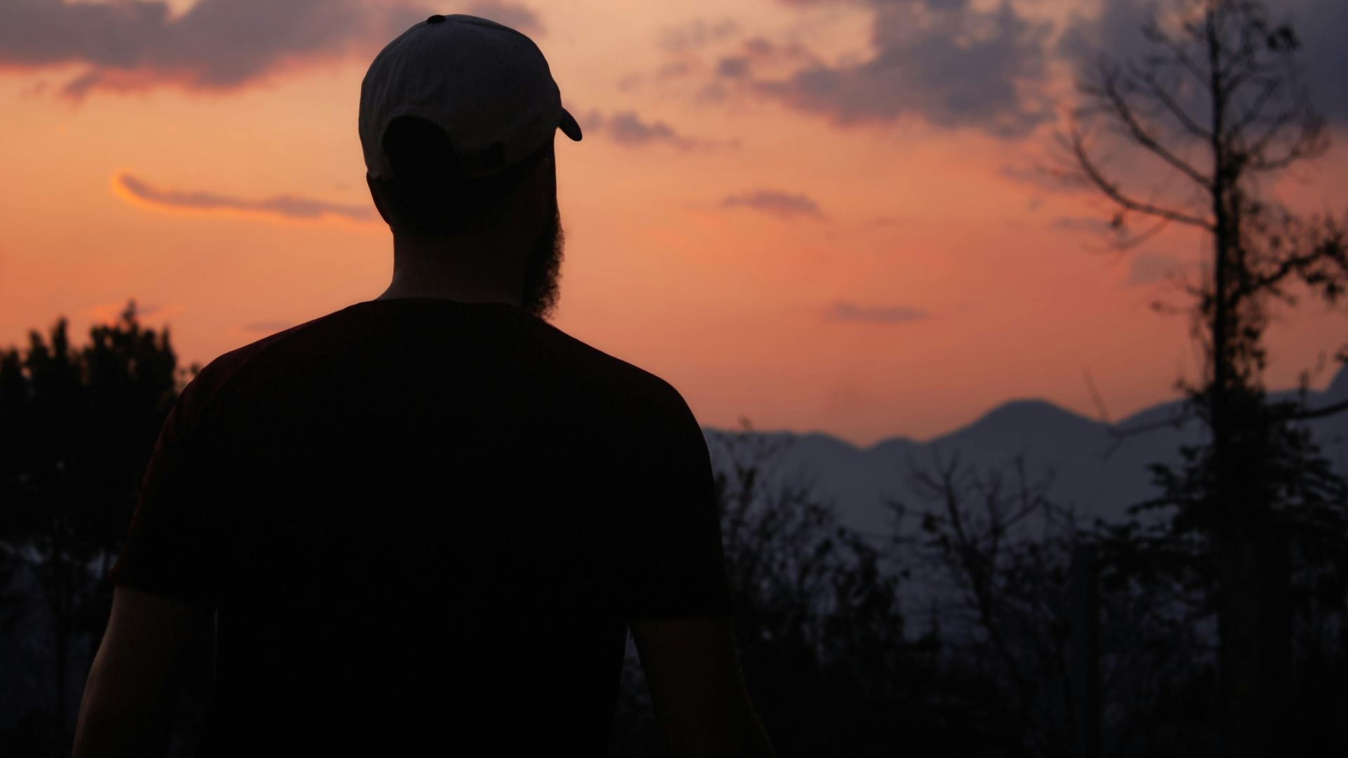 A peaceful silhouette of a man gazing at a vibrant sunset over mountains, conveying tranquility.