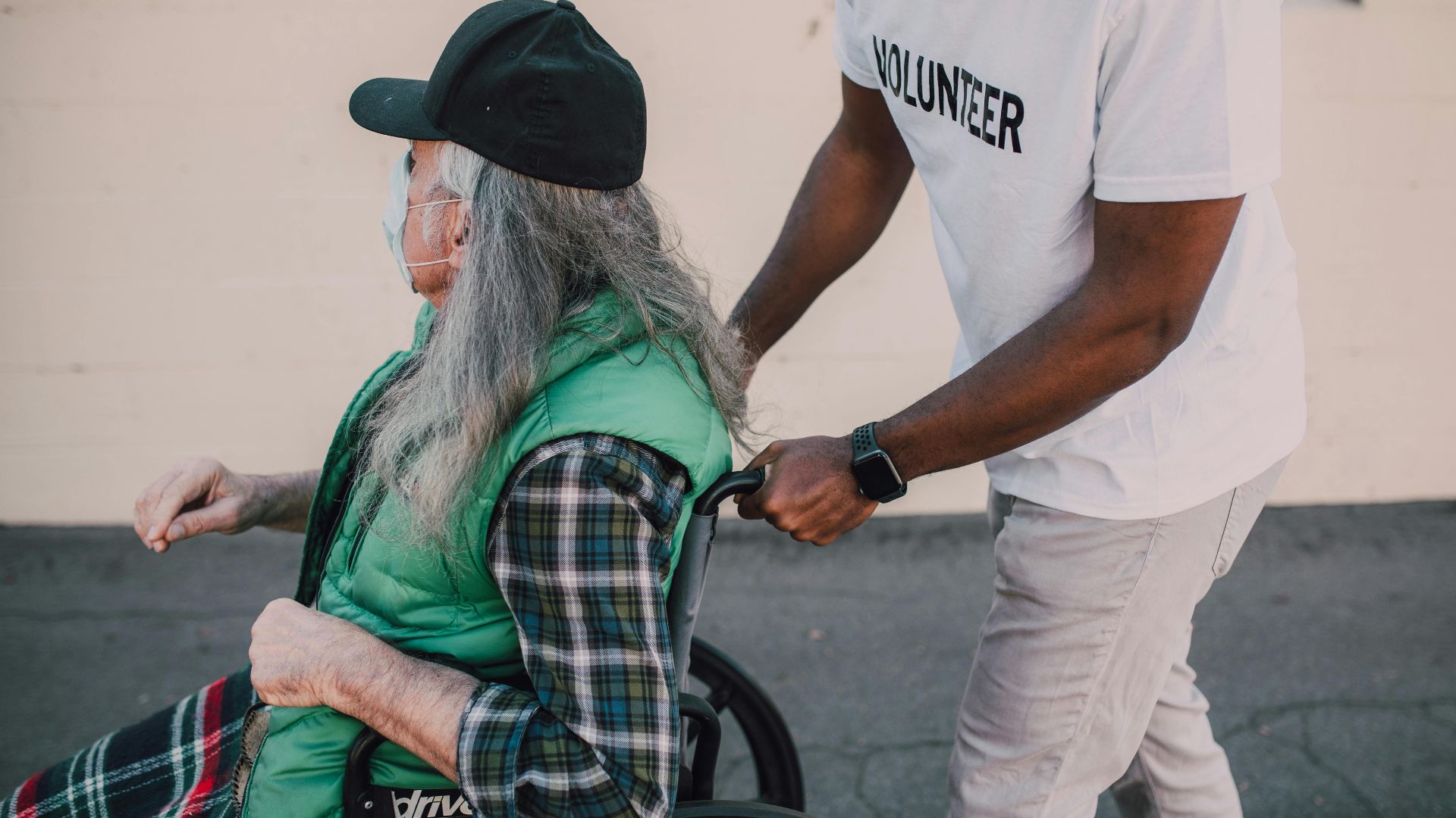 A volunteer helps a senior in a wheelchair during daytime outdoors.