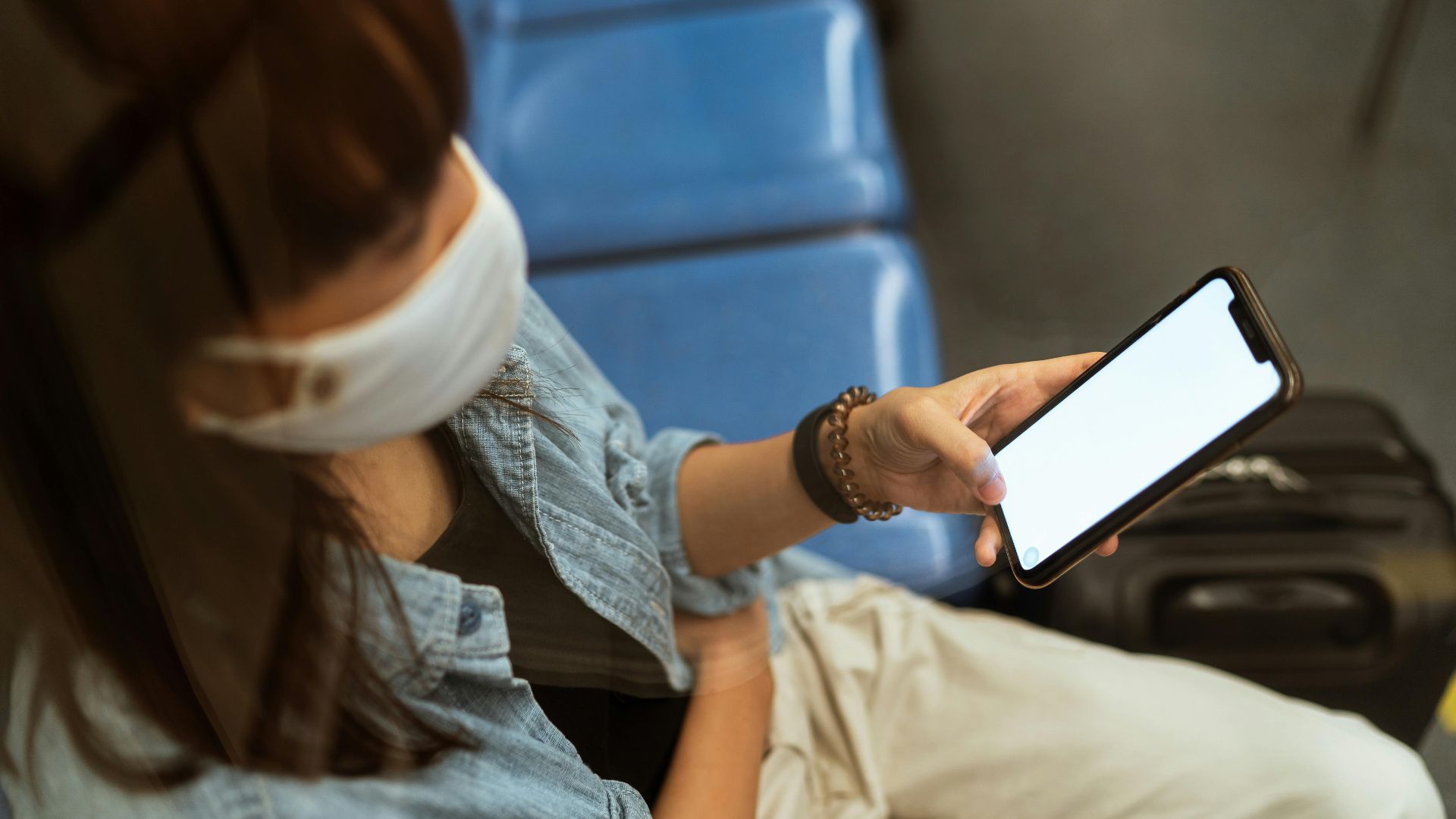 A woman wearing a mask browses her smartphone while traveling in public transportation during a pandemic.