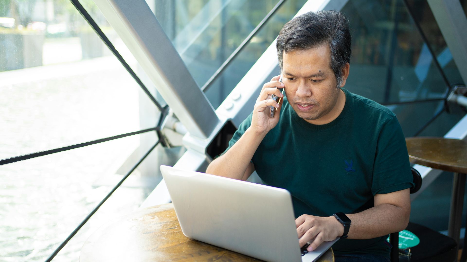 Asian man multitasking on laptop and phone in Bangkok café.