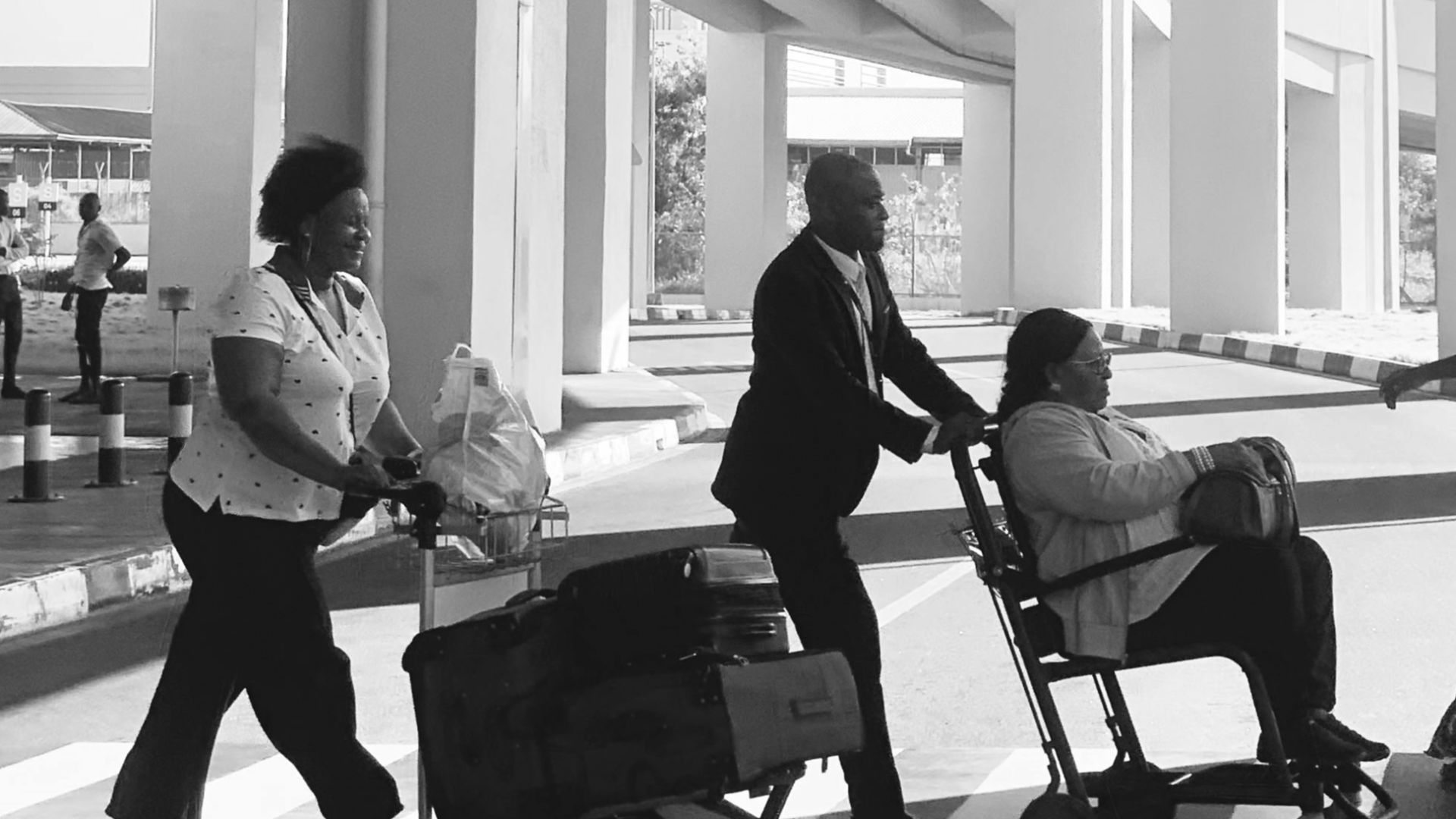 Black and white photo of people crossing at Accra airport with a stark architectural backdrop.