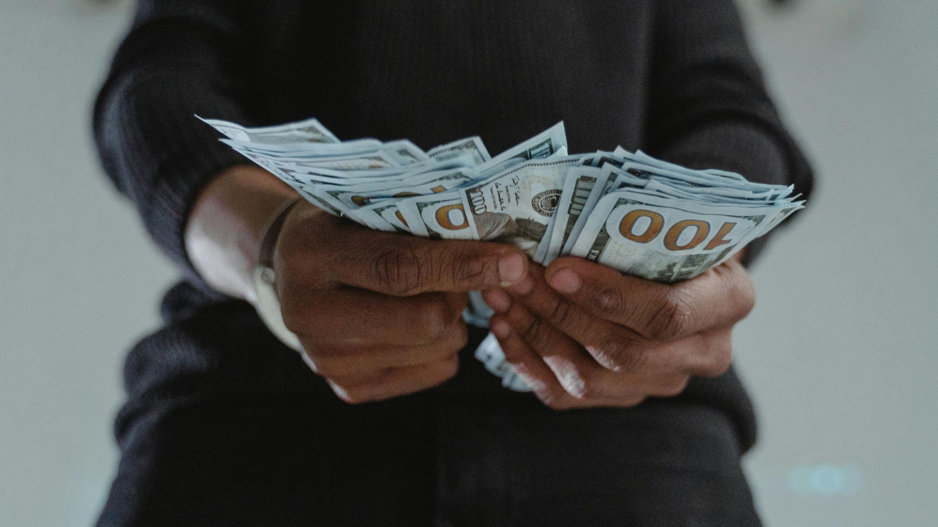A close-up view of a person holding a stack of US hundred dollar bills indoors.