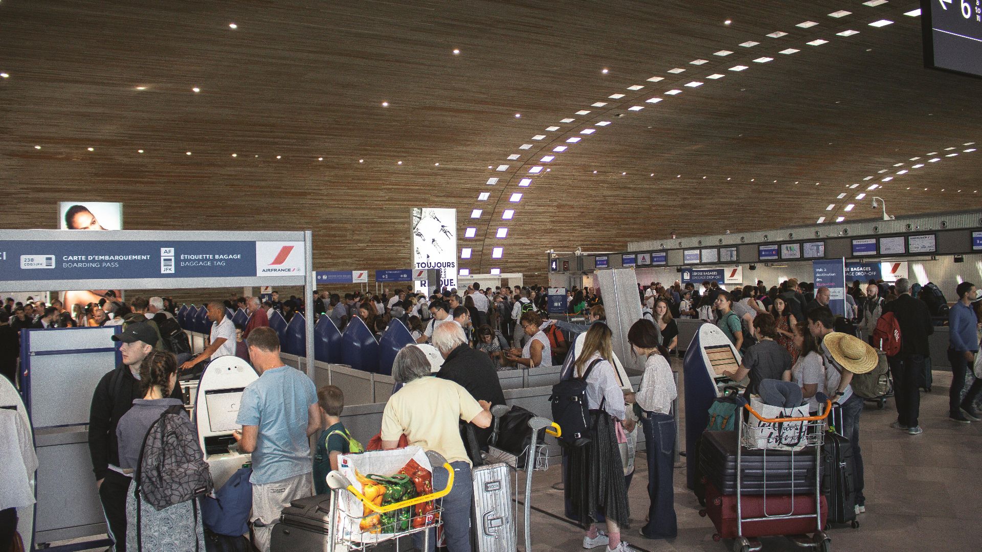 Crowded airport terminal with travellers in line. Indoor setting with modern architecture.