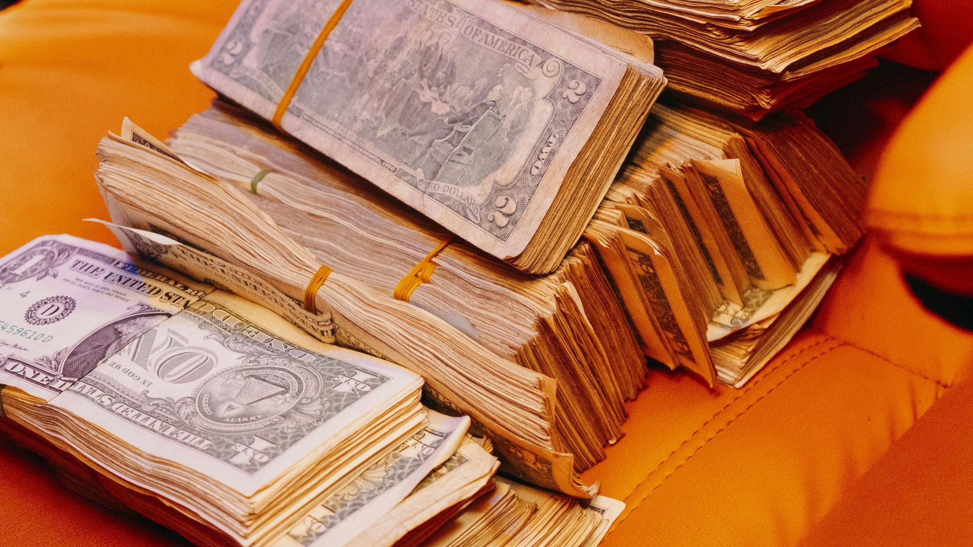 Close-up of bundled currency notes on a vibrant orange leather seat, symbolizing wealth.