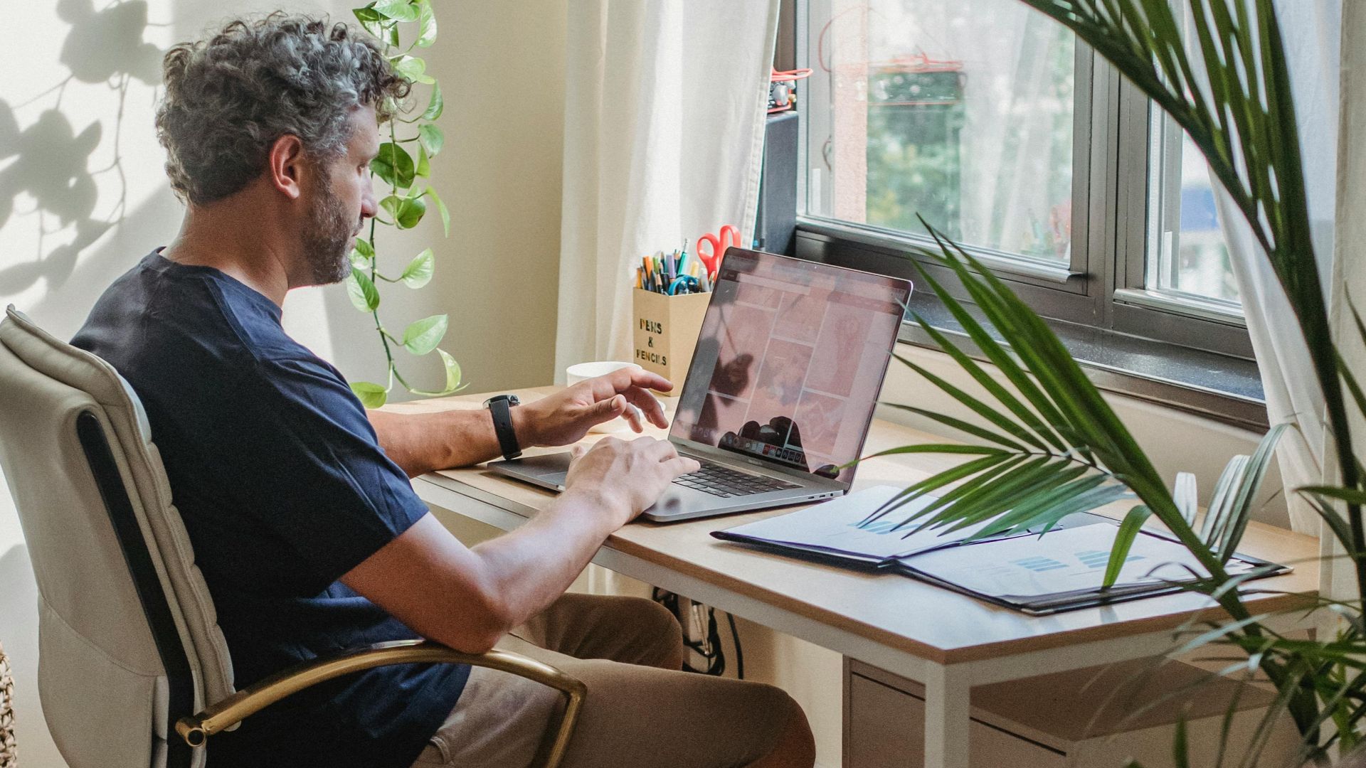 Confident adult husband in home clothes remote working on laptop while crop unrecognizable wife sitting on couch and knitting in cozy apartment in daytime