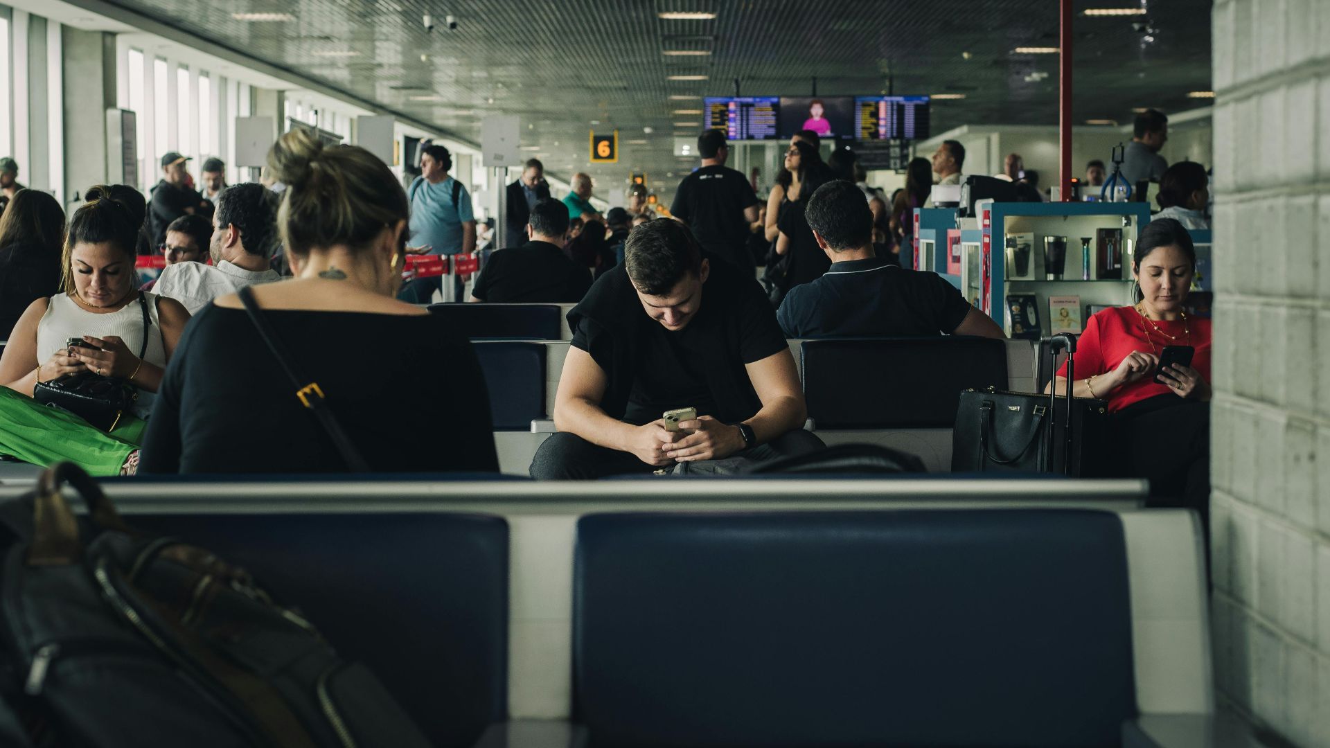 Travelers seated and waiting at São Paulo airport terminal, engaging with smartphones.