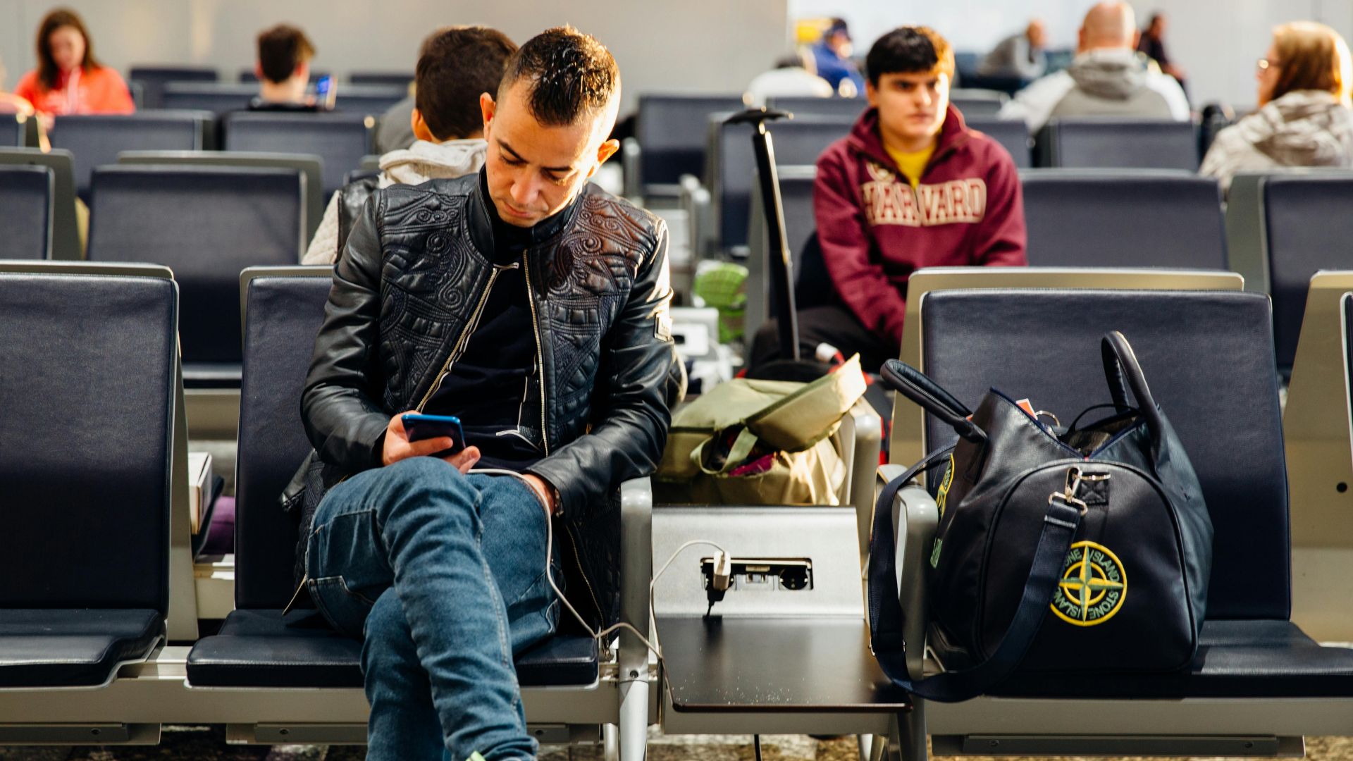 People sitting in an airport lounge, focused on smartphones and waiting for flights.