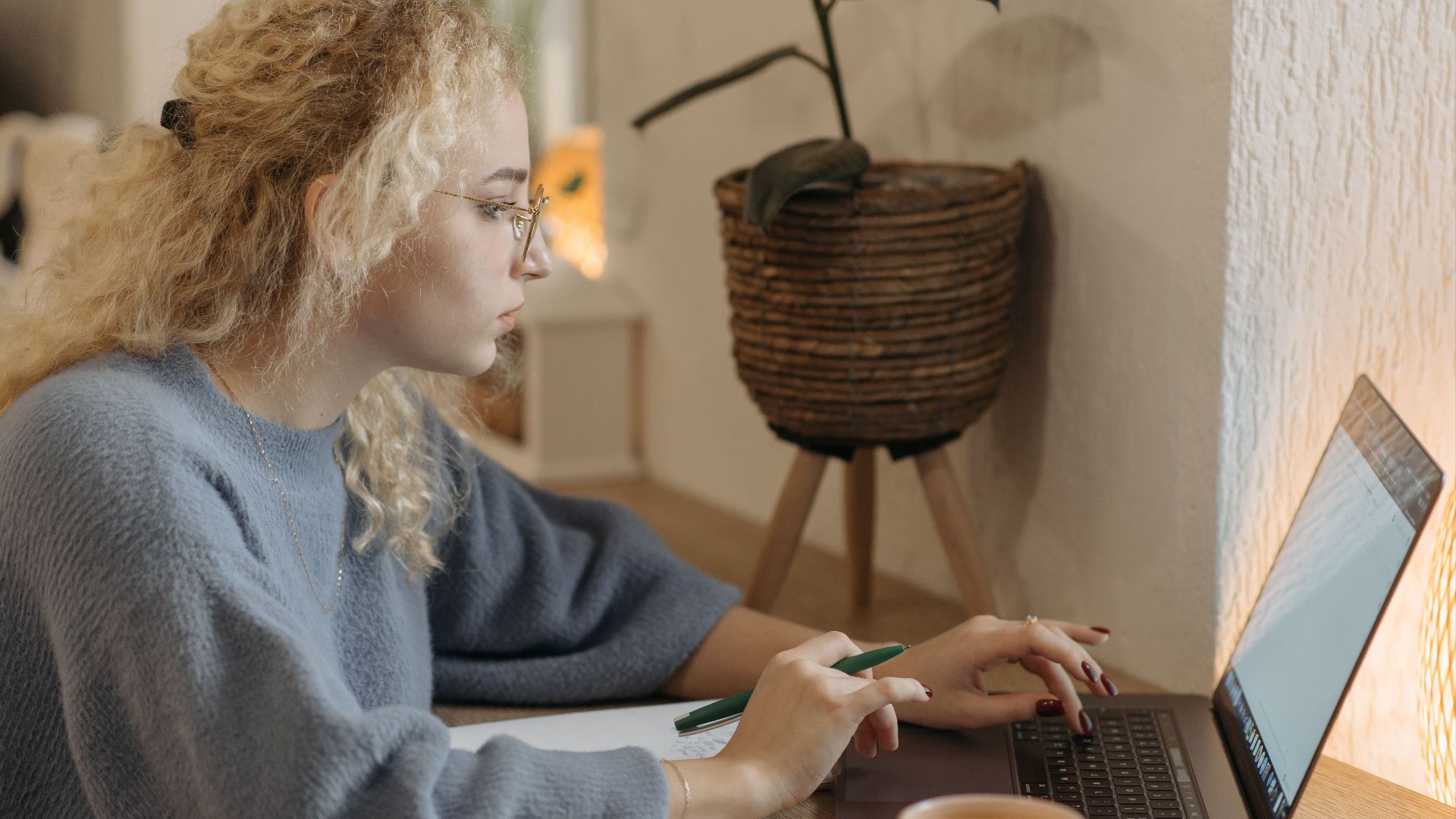 Young woman focused on remote work in a cozy indoor setting with a laptop and coffee cup.