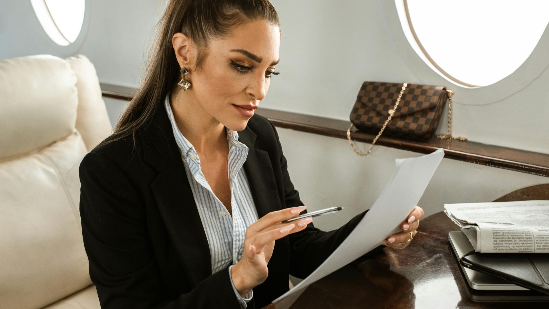 Woman in formal attire reviewing documents on a private jet. Luxurious air travel setting.
