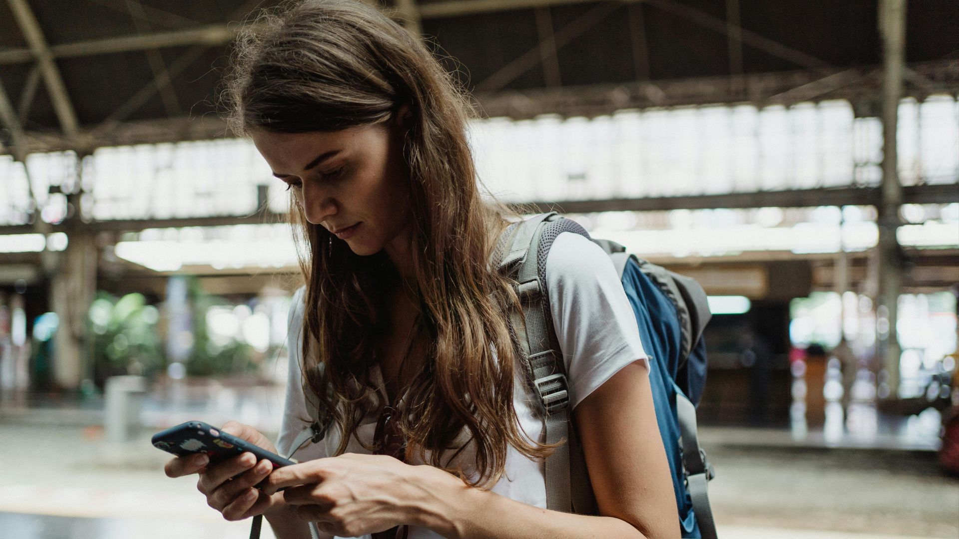 A young woman checks her smartphone while traveling at a train station.