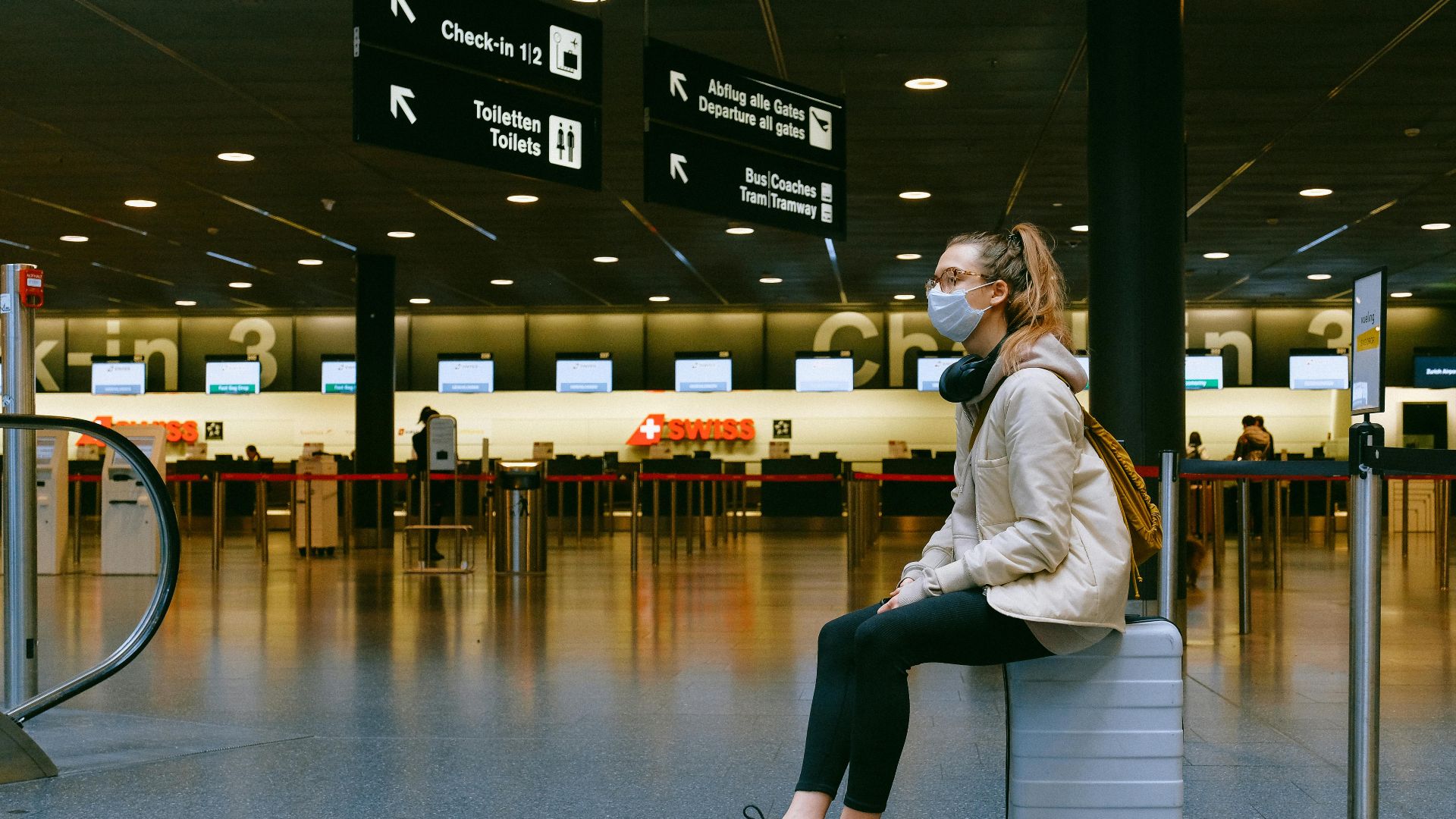 A woman wearing a face mask sits on luggage in an airport terminal amid the pandemic.