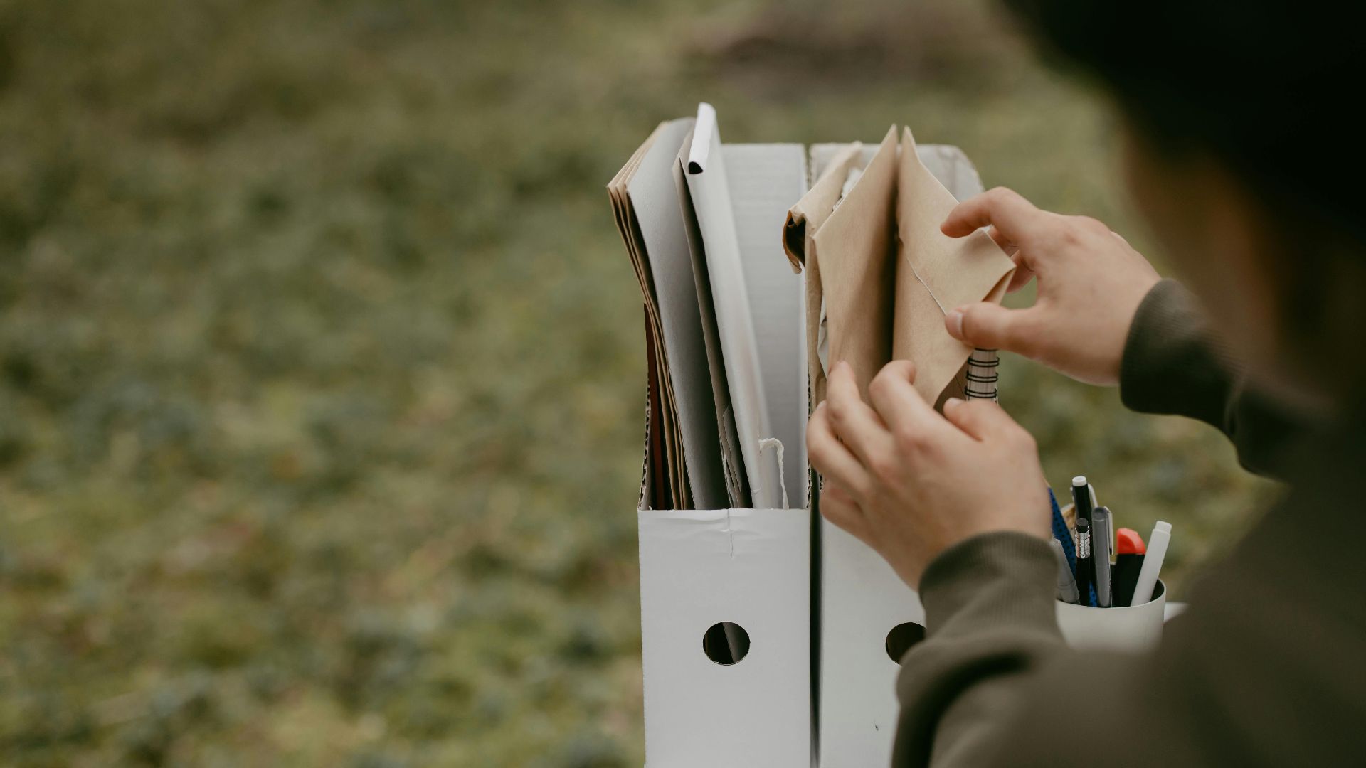 Person sorting documents in folders outdoors, hands visible, neutral tone.