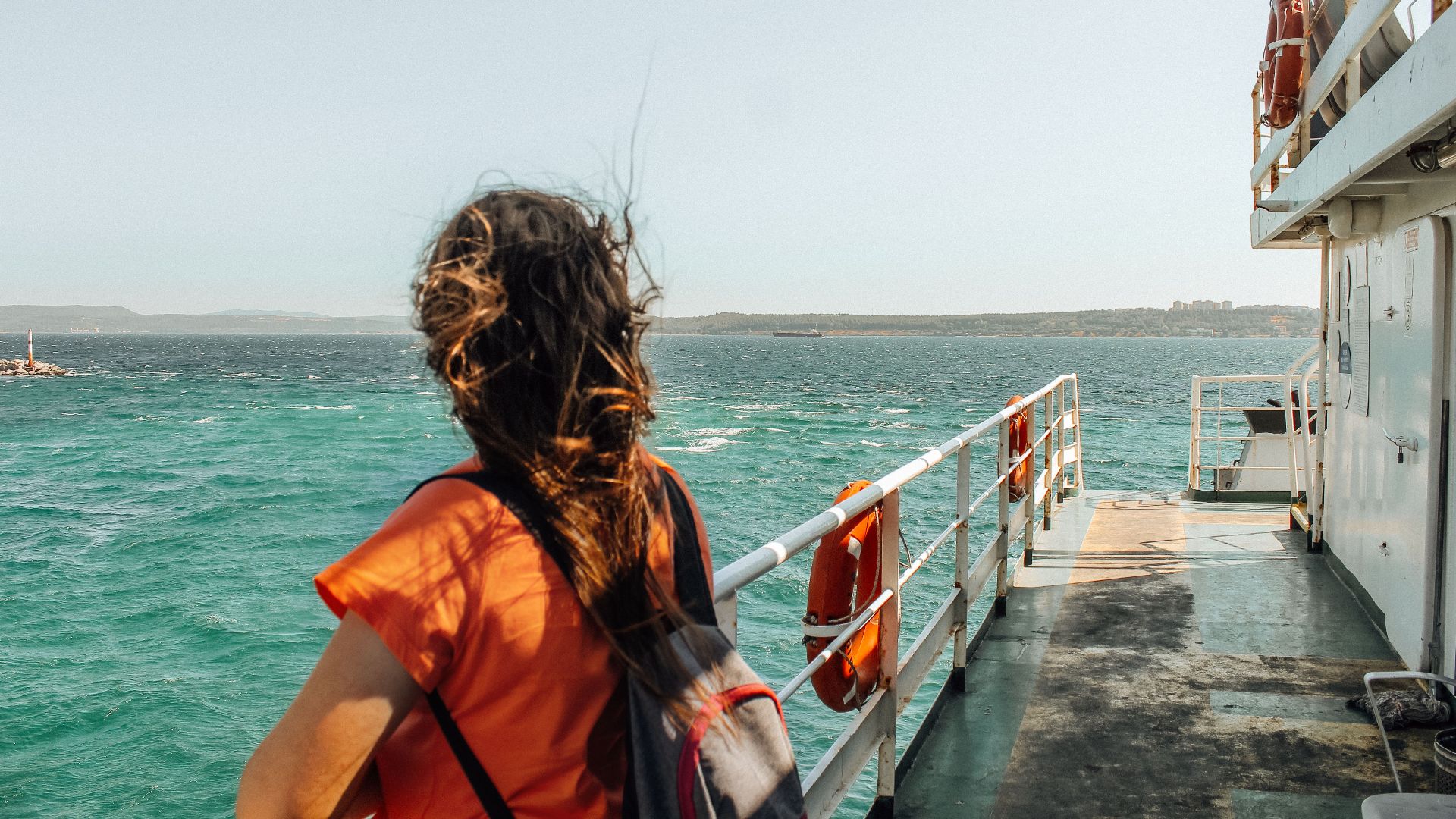 A brunette woman stands on a ferry deck enjoying the ocean view. Perfect for travel and leisure themes.