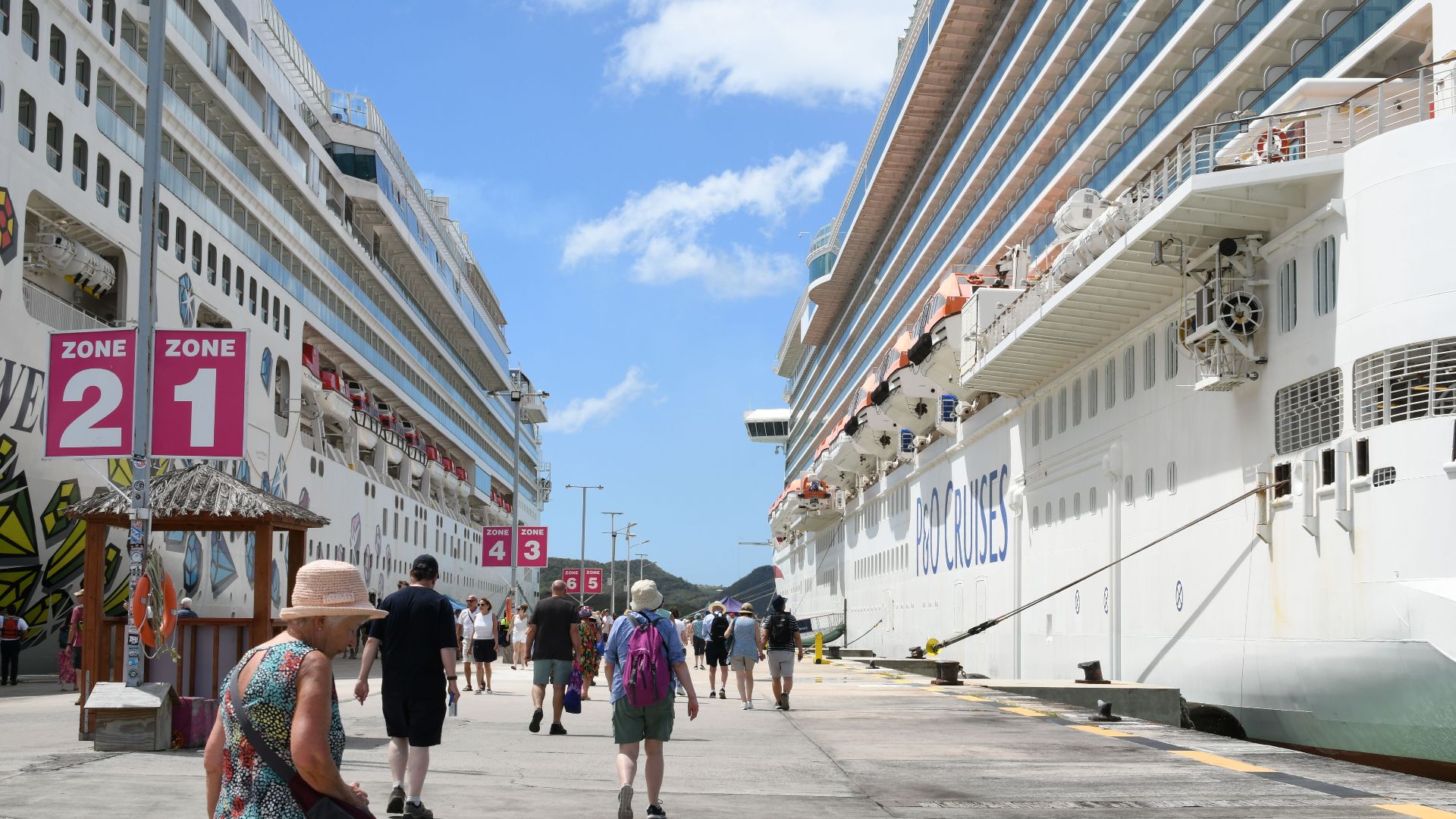 Bustling cruise port with tourists, featuring two large cruise ships under a bright blue sky.
