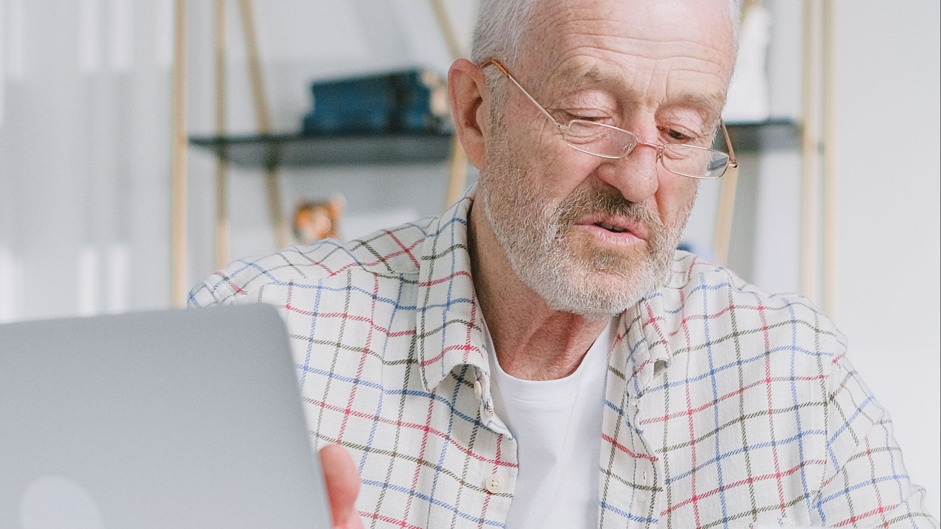 Elderly man reading papers at home with a laptop, emphasizing financial planning.