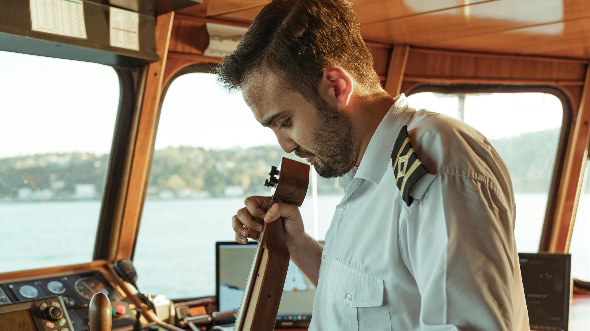 A ship captain seated in the bridge, playing guitar, creating a relaxed maritime atmosphere.