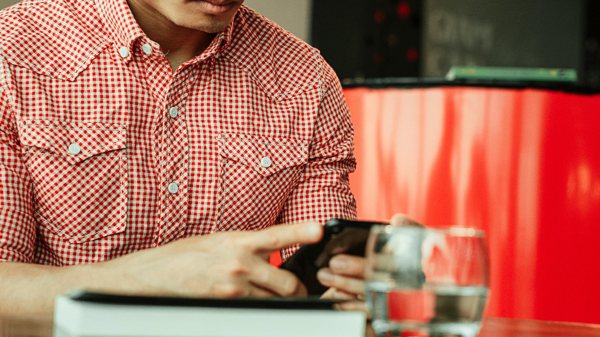Man wearing glasses focused on using smartphone indoors with a modern setting.