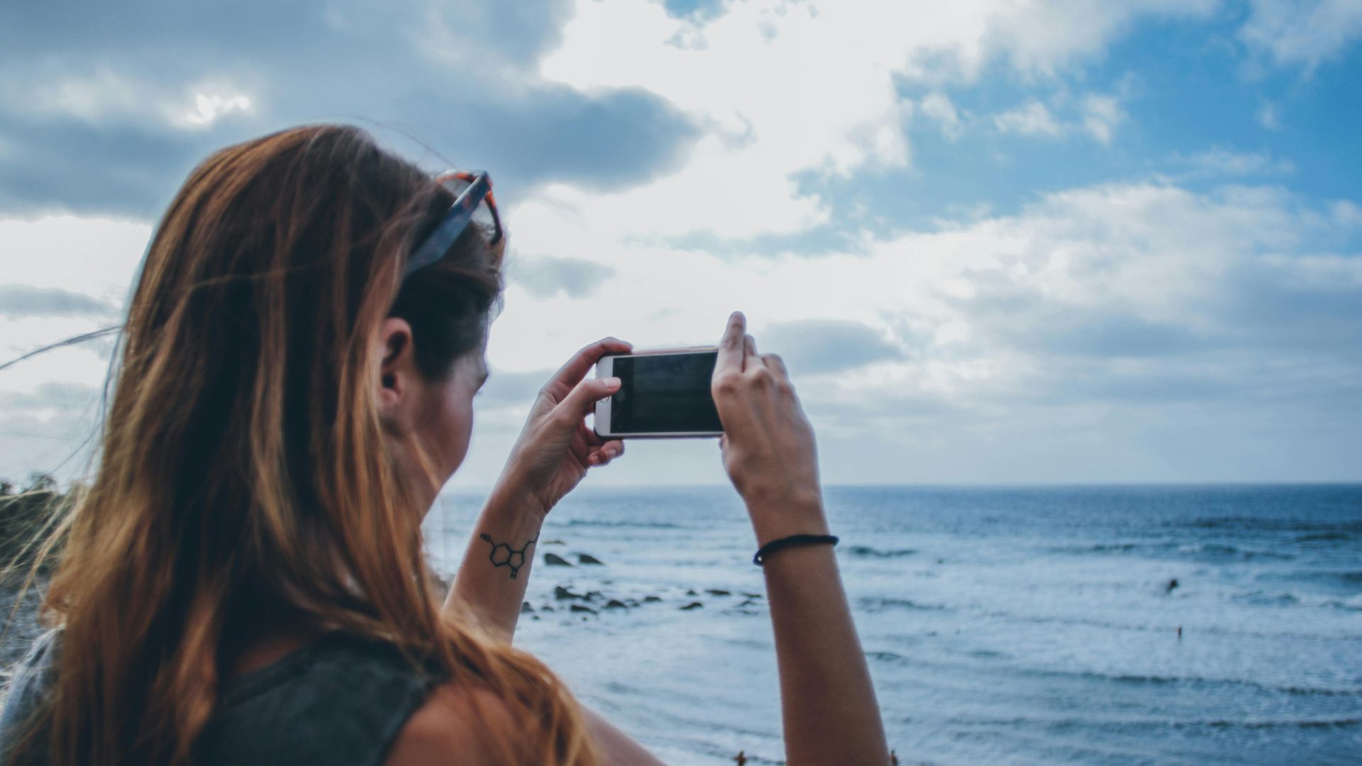A woman uses her smartphone to capture a stunning seascape, showcasing the vast ocean and sky.