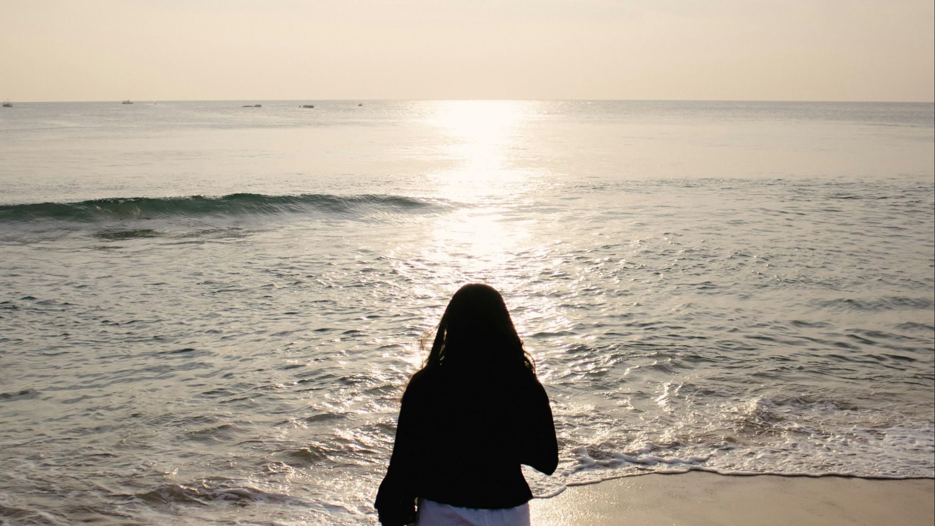 A solitary figure walks along a tranquil beach at sunrise, capturing a peaceful moment.