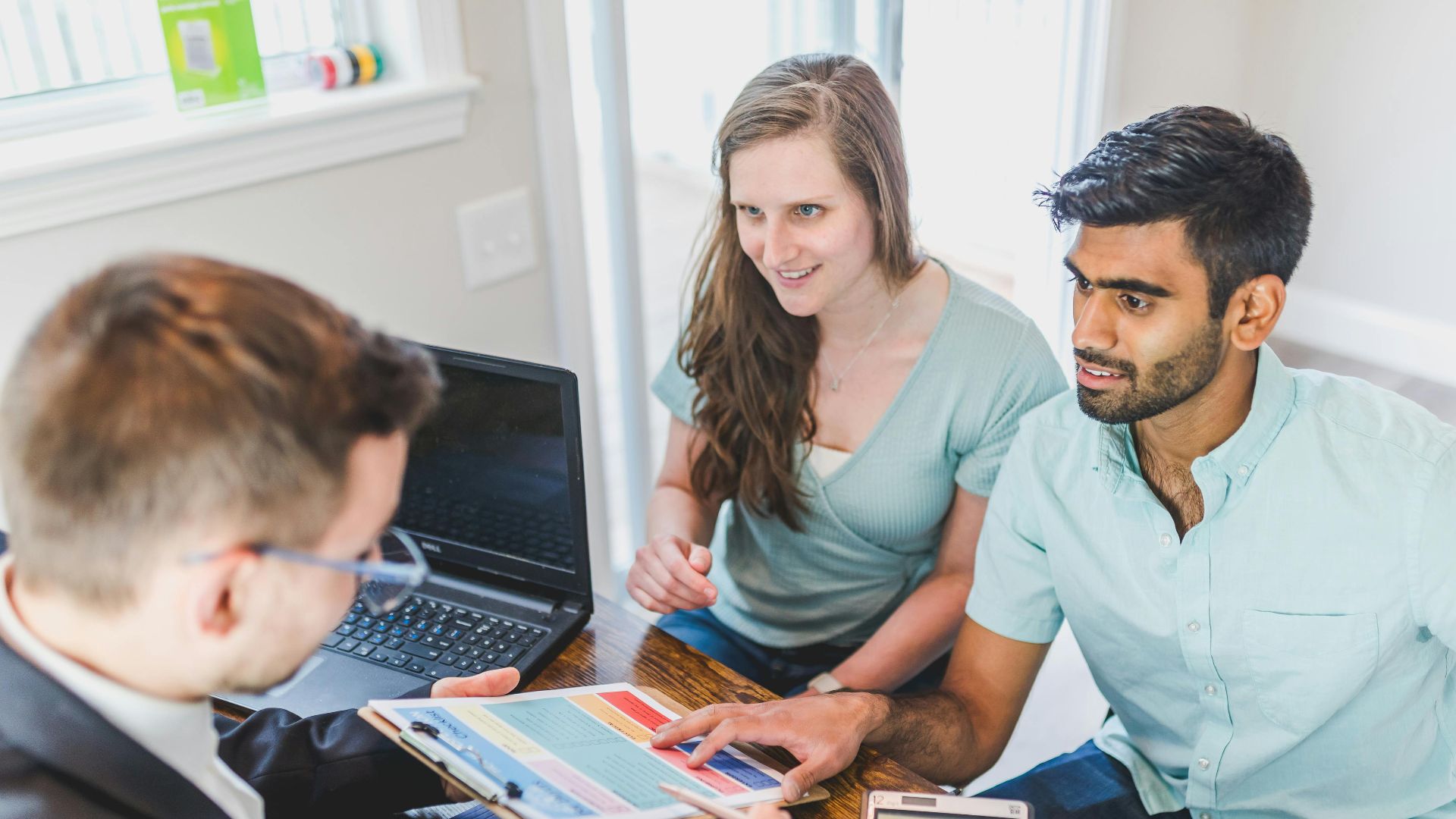 A couple consults with a real estate agent about buying a new home, papers and calculator on the table.