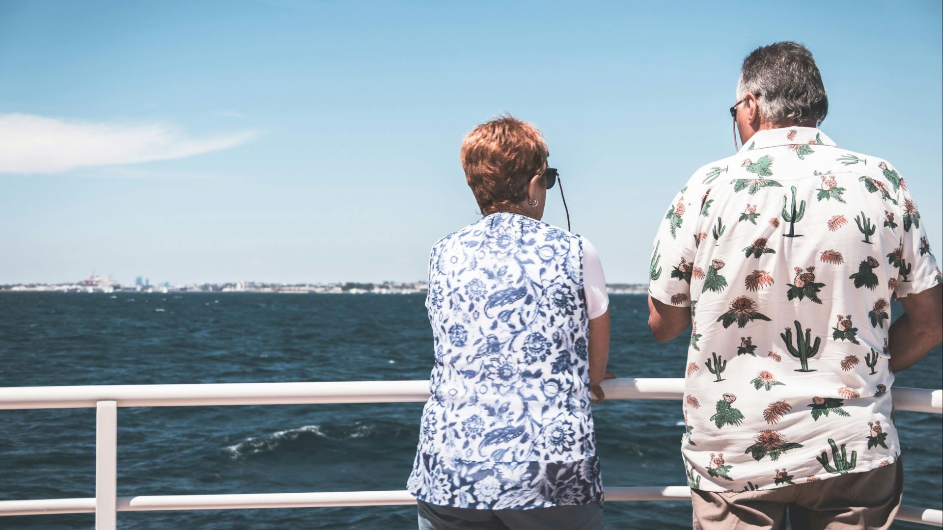Back view of unrecognizable mature male and female travelers in casual clothes and sunglasses admiring sea during cruise on boat on sunny day