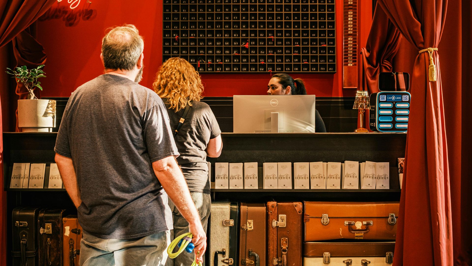 A couple with a dog checks in at a stylish, vintage hotel front desk.