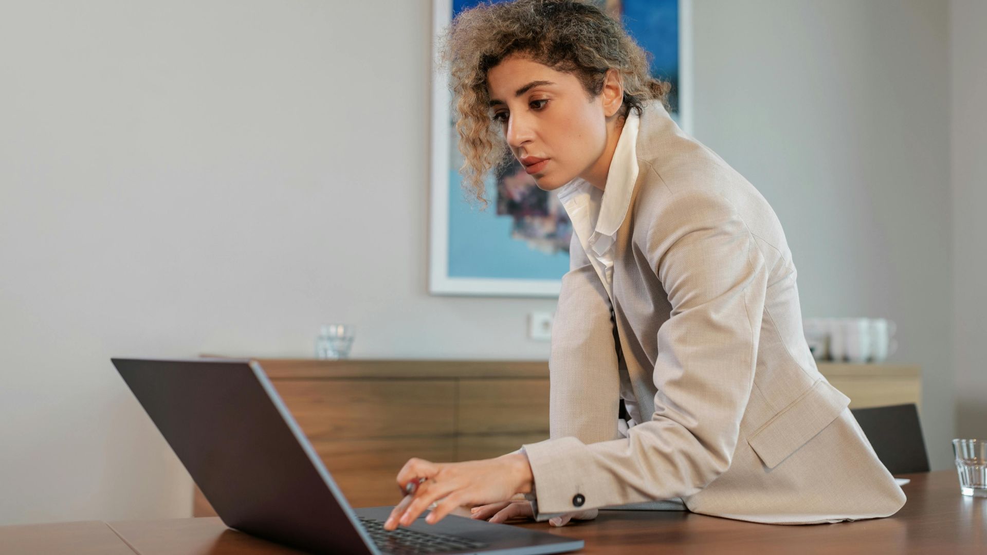Businesswoman in a beige blazer working on a laptop at a modern office desk.