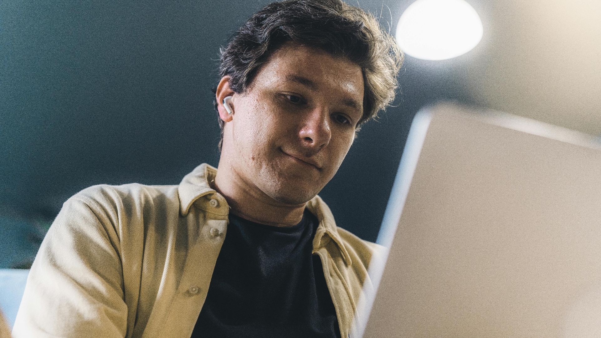 Young man working on a laptop indoors, smiling and focused, representing a modern freelance lifestyle.