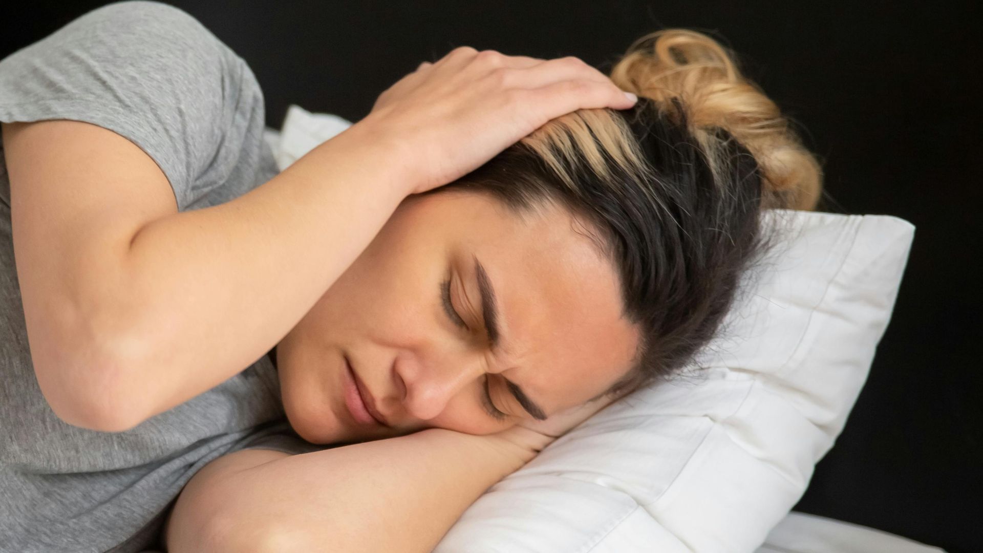 A woman looks frustrated in bed as her partner snores loudly, highlighting sleep disturbance issues.