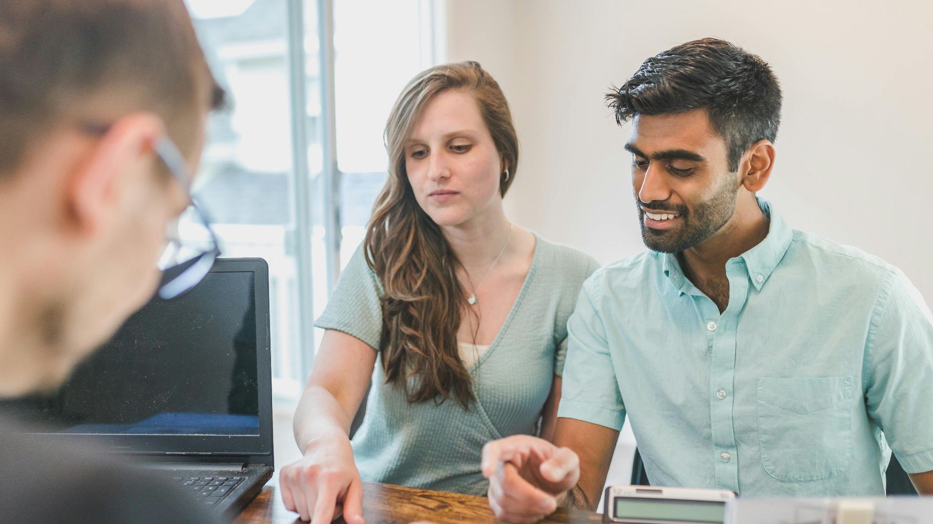 Young couple consulting with a financial advisor using a calculator and documents in a bright office setting.