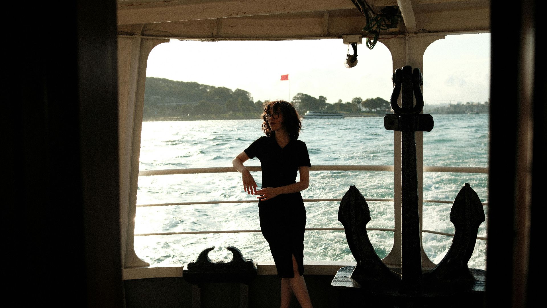 A woman in a black dress enjoys a relaxing moment on a ferry overlooking the sea.