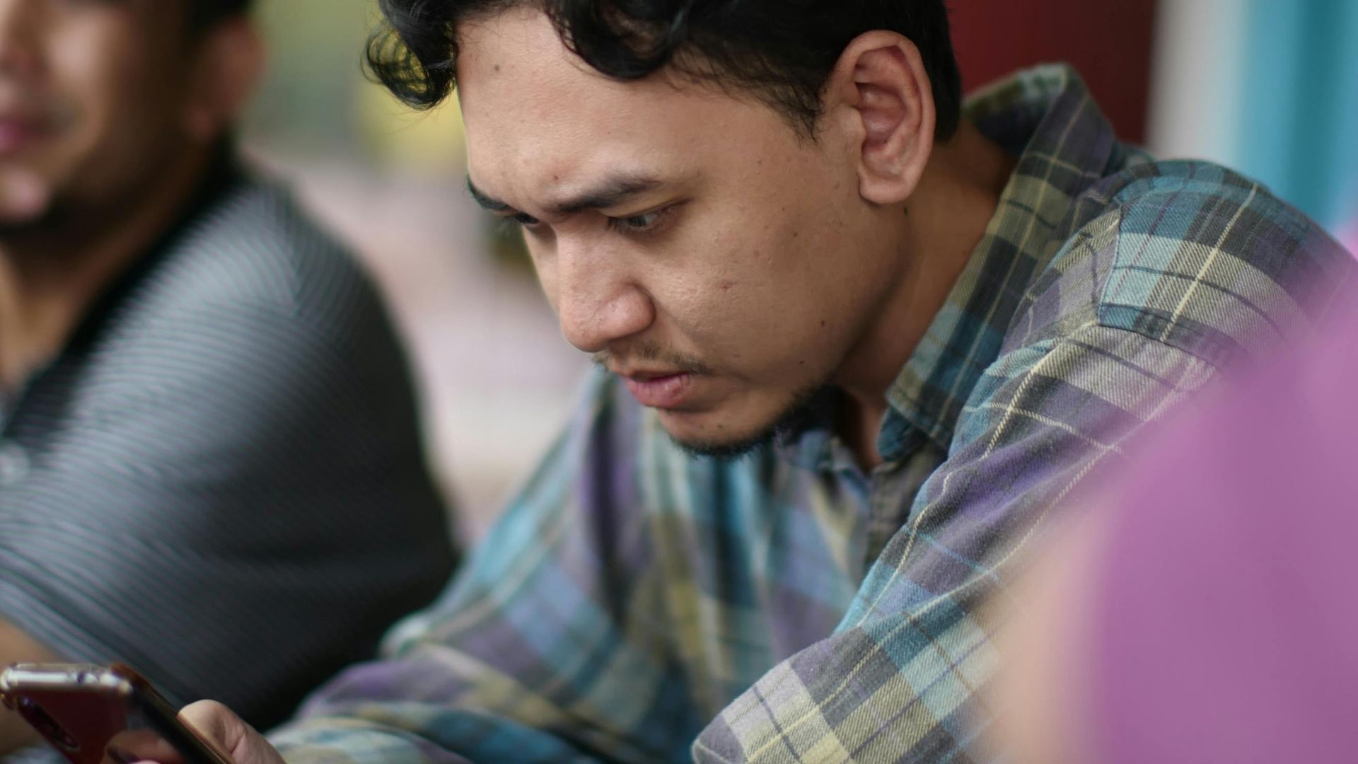 Young man focused on smartphone in a lively Kuala Dungun cafe setting.