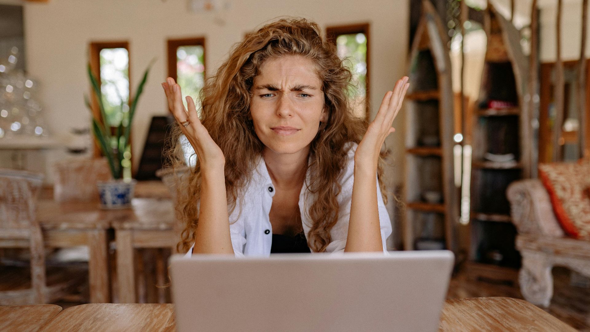 A woman frustrated with her laptop while working remotely indoors, expressing stress.
