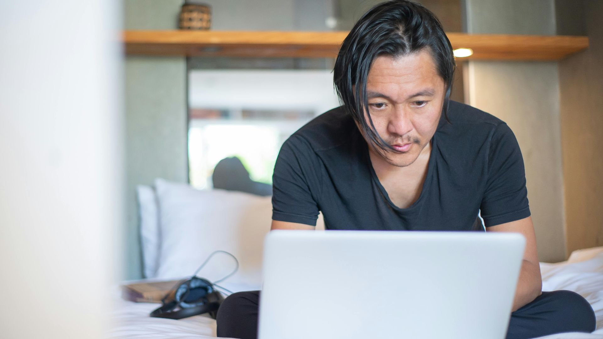 An Asian man working from home on a laptop, focusing on his digital tasks in a cozy indoor setting.